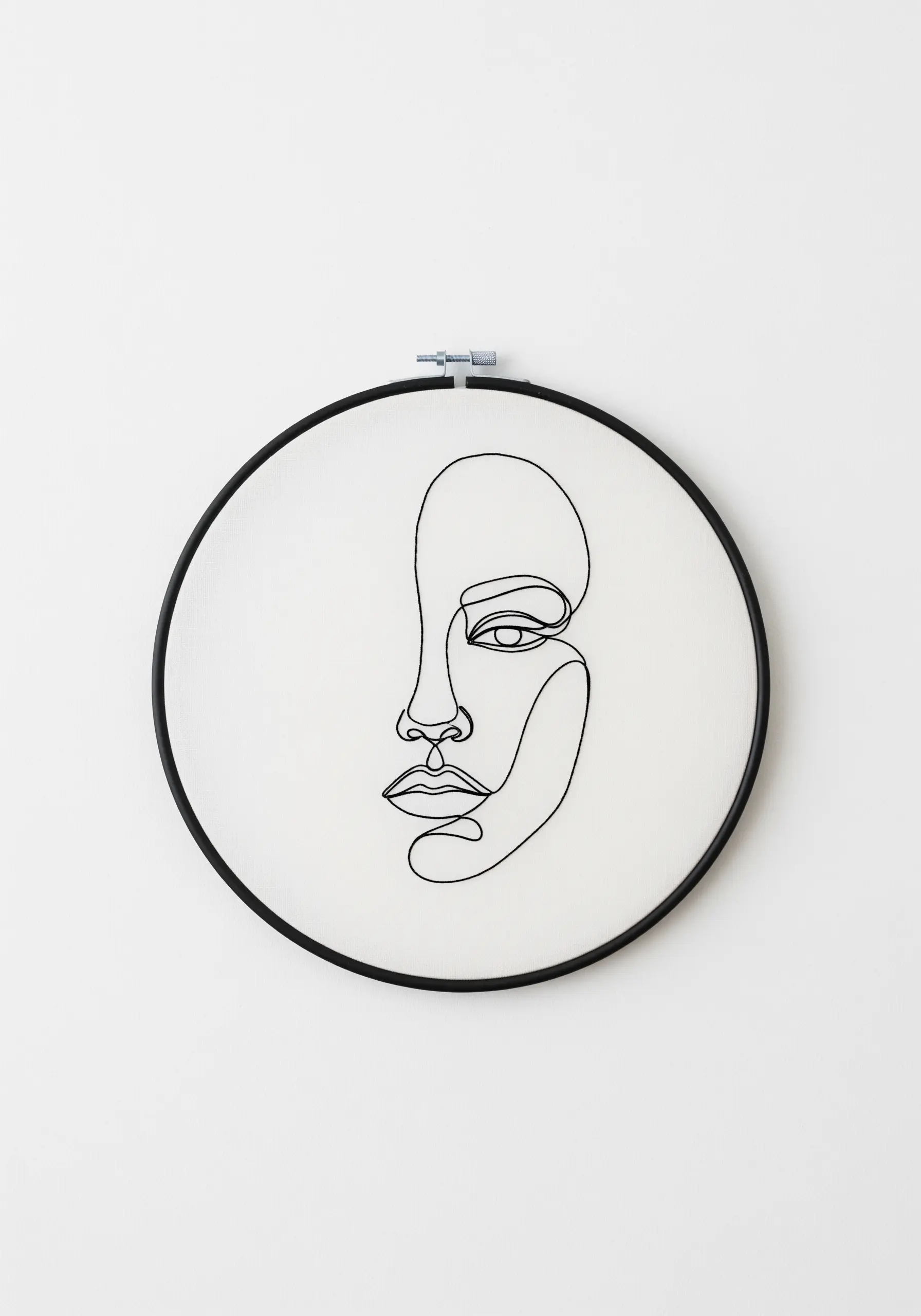 A minimalist single-line art portrait of a face, stitched in black thread on white fabric.
