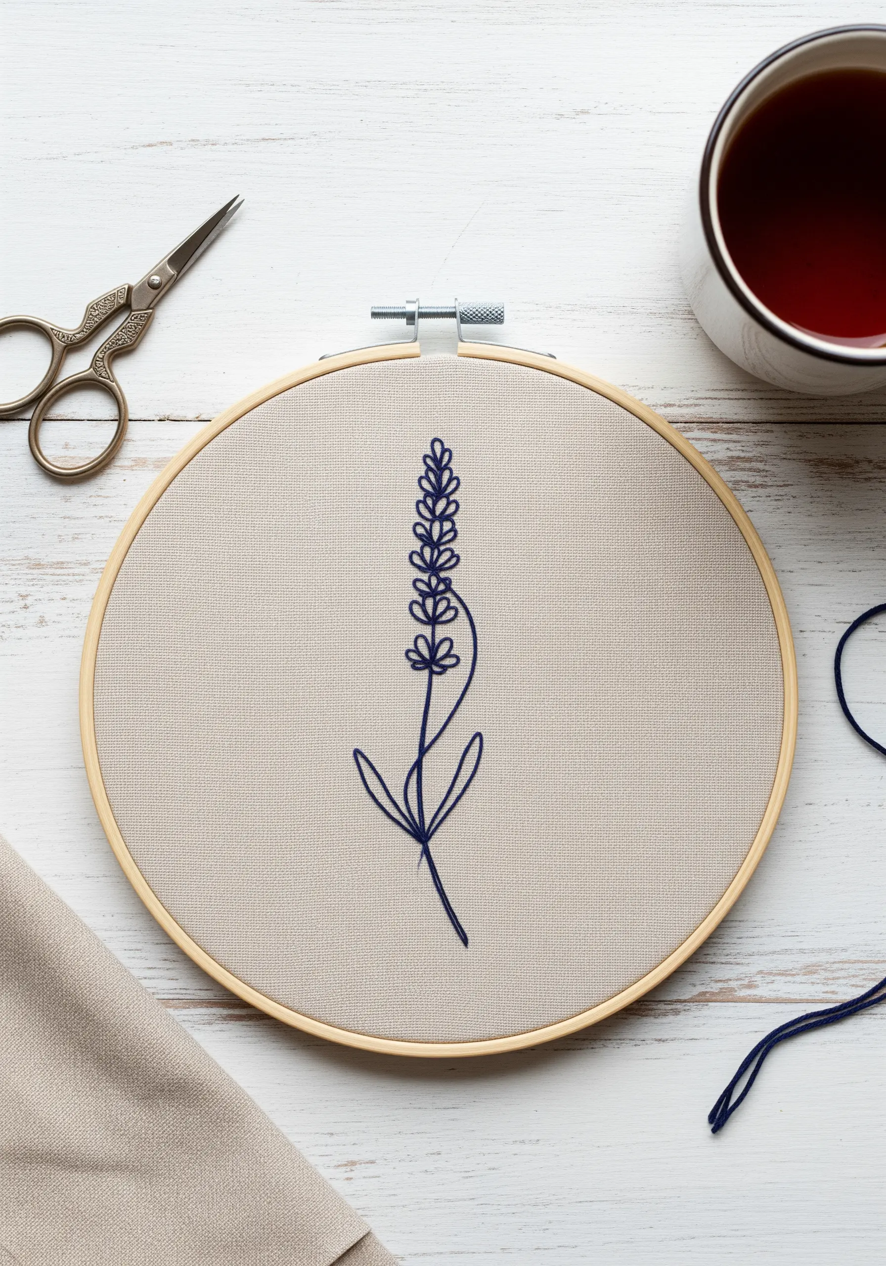 Single-line lavender motif stitched in navy blue thread on neutral fabric in a hoop.