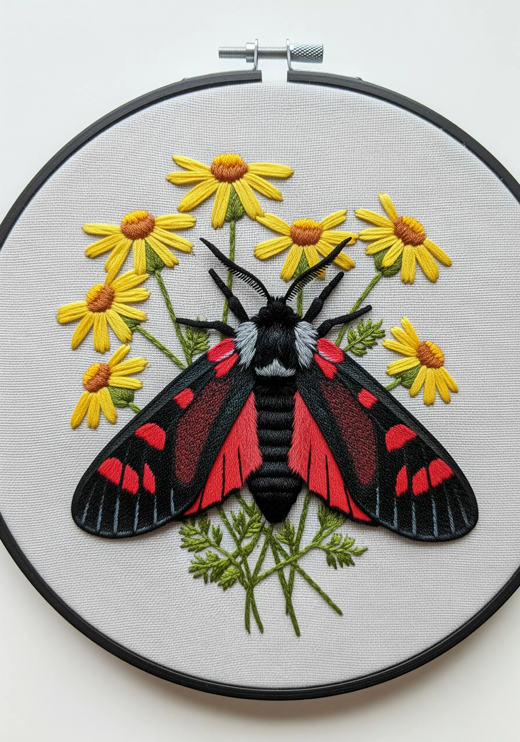 A black and red Cinnabar moth embroidered with yellow daisies on a light gray background.