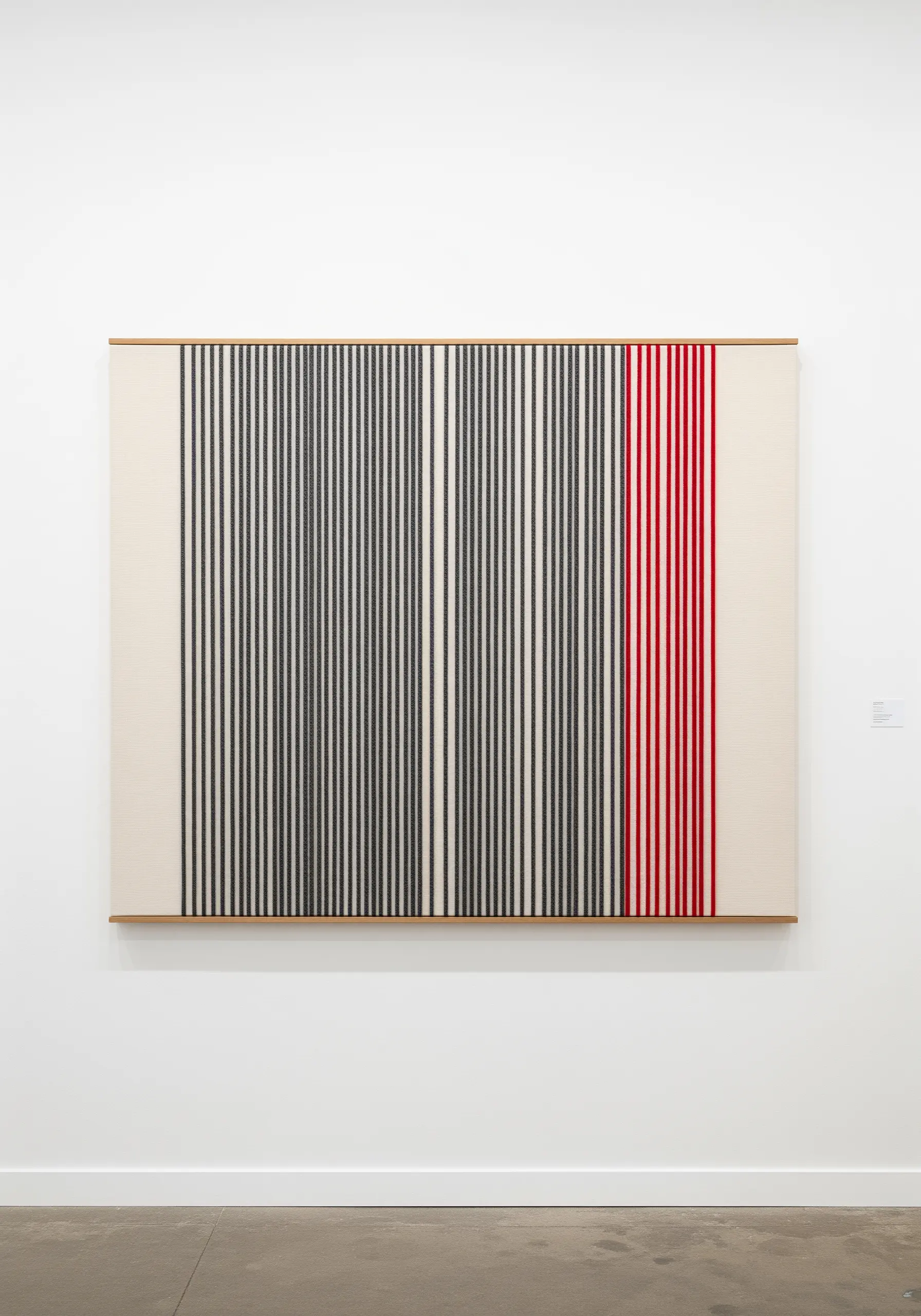 Large-scale fiber art with vertical black, white, and red threads stretched across a frame.