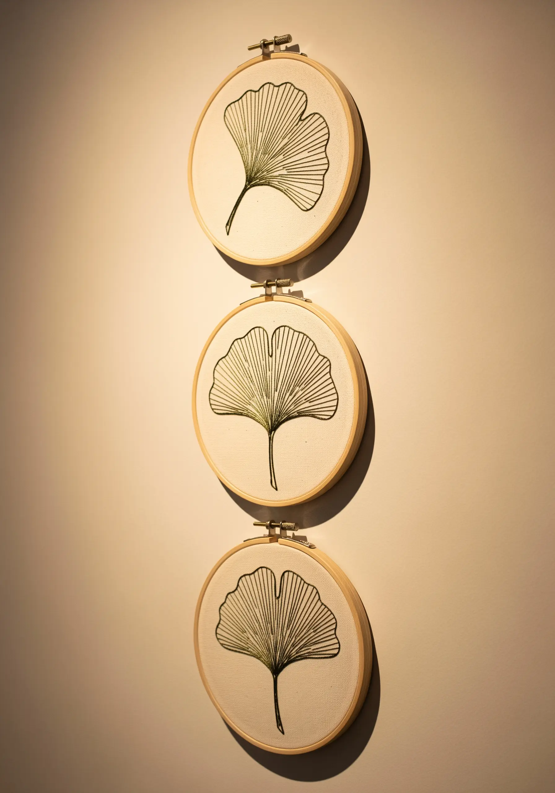 Triptych of three embroidery hoops, each featuring a delicate ginkgo leaf in green thread.