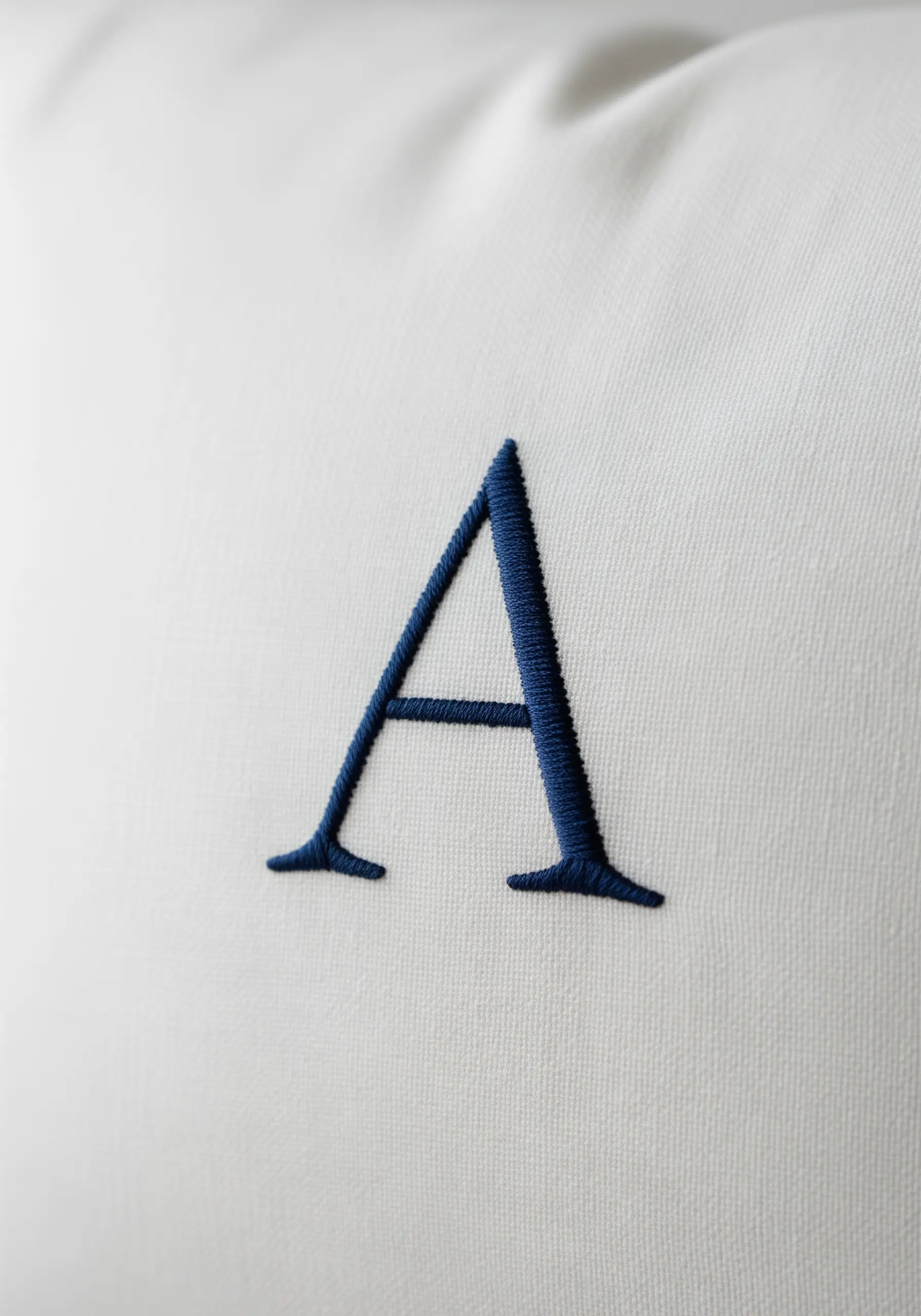 A perfectly executed navy blue monogram 'A' in padded satin stitch on a white pillow.