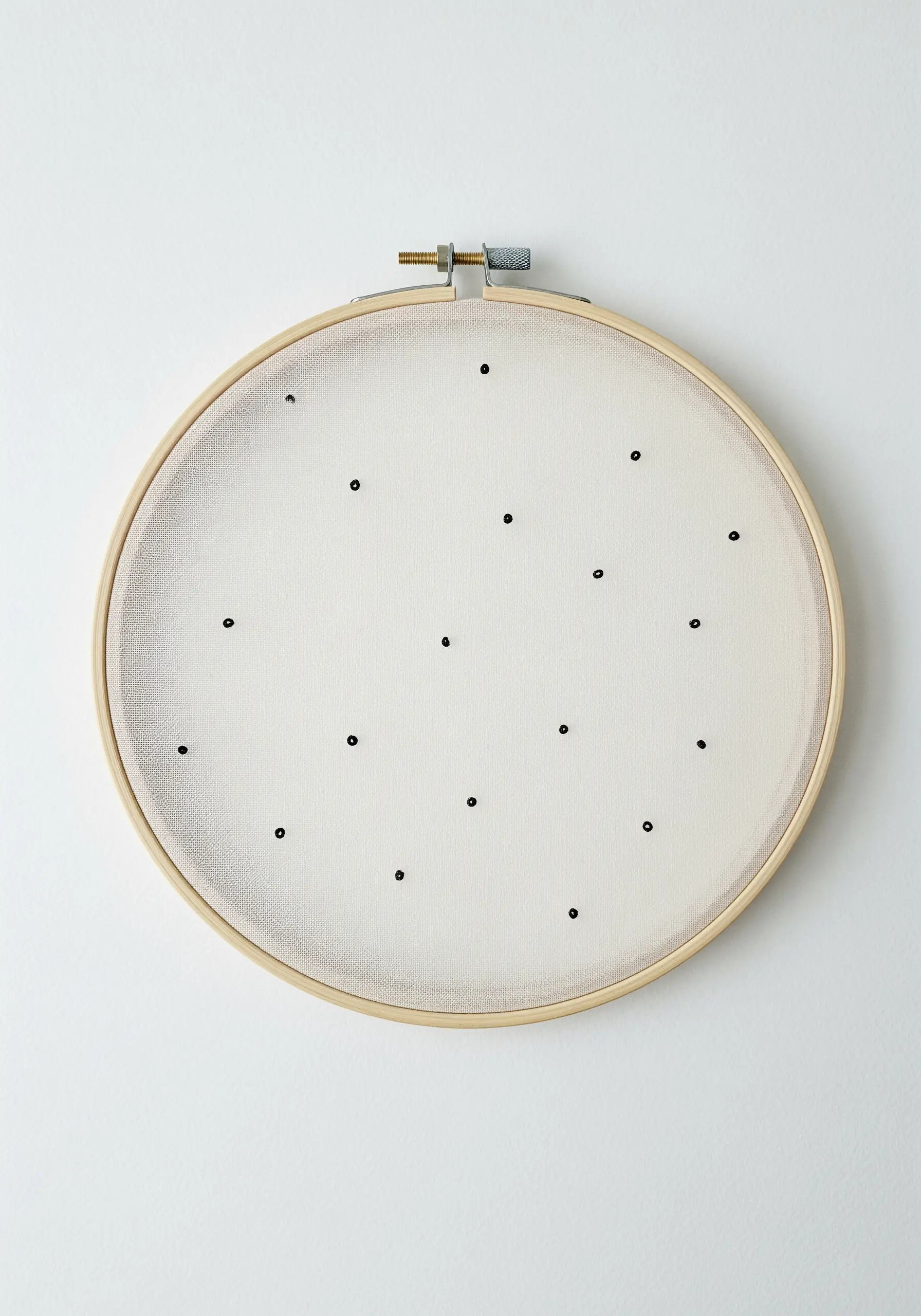 Minimalist hoop art with small, scattered black stitches on a wide expanse of white fabric.