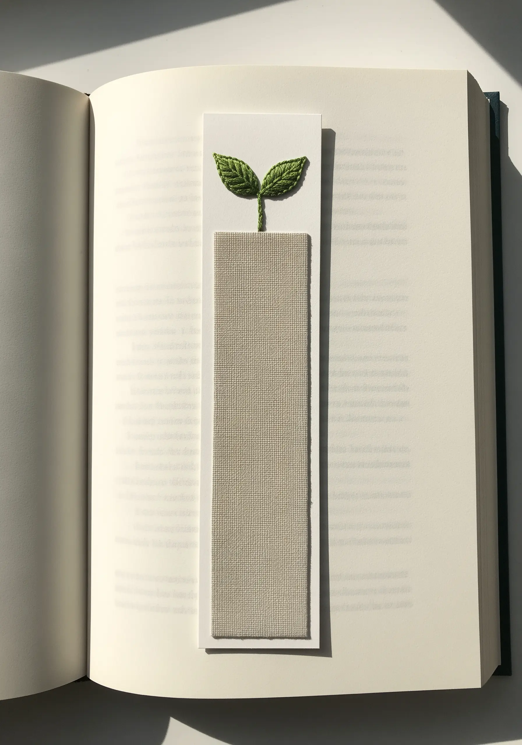 A minimalist bookmark topped with two small, perfectly satin-stitched green leaves.