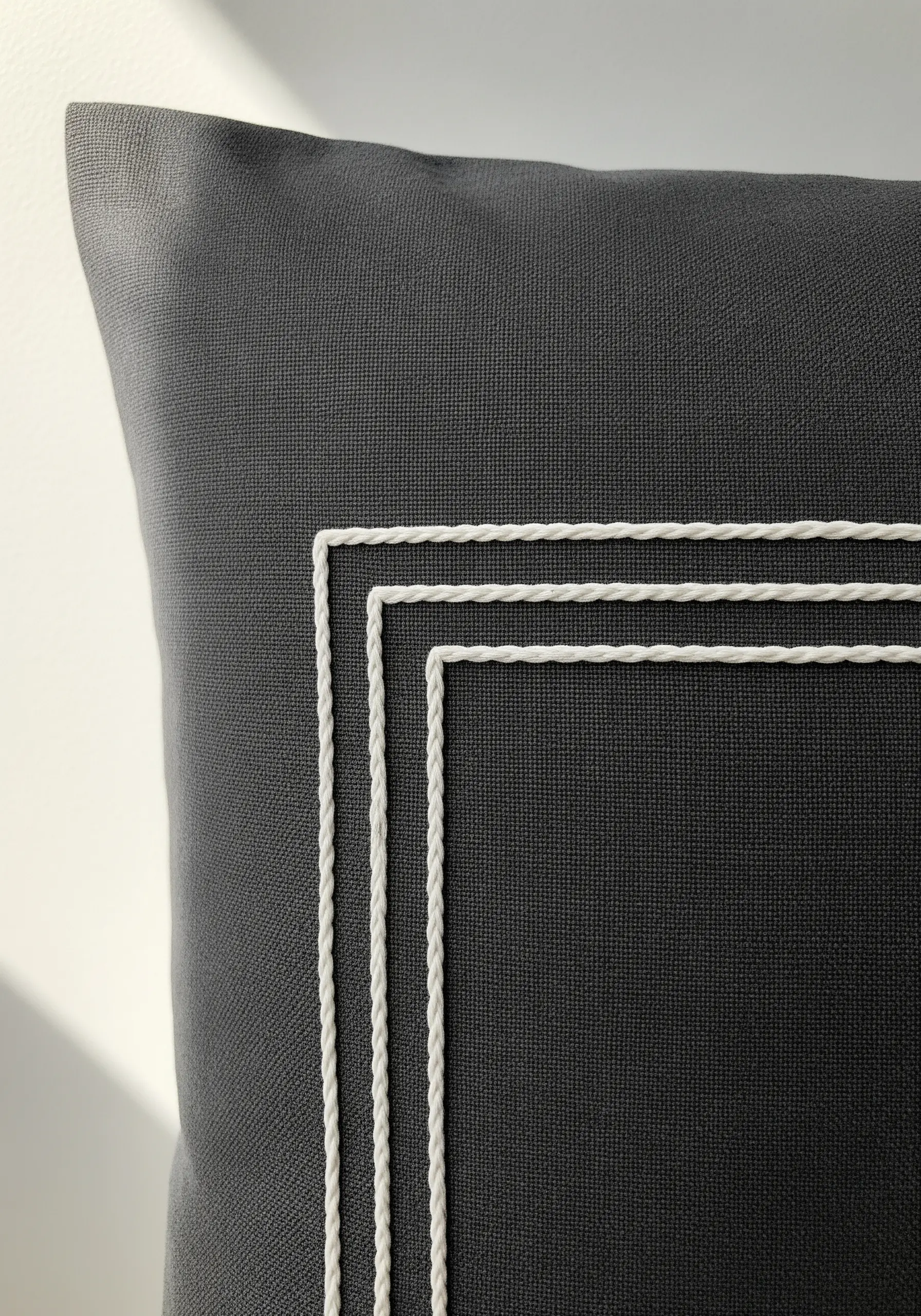 White couched cord embroidery forming a geometric border on a dark grey pillow.