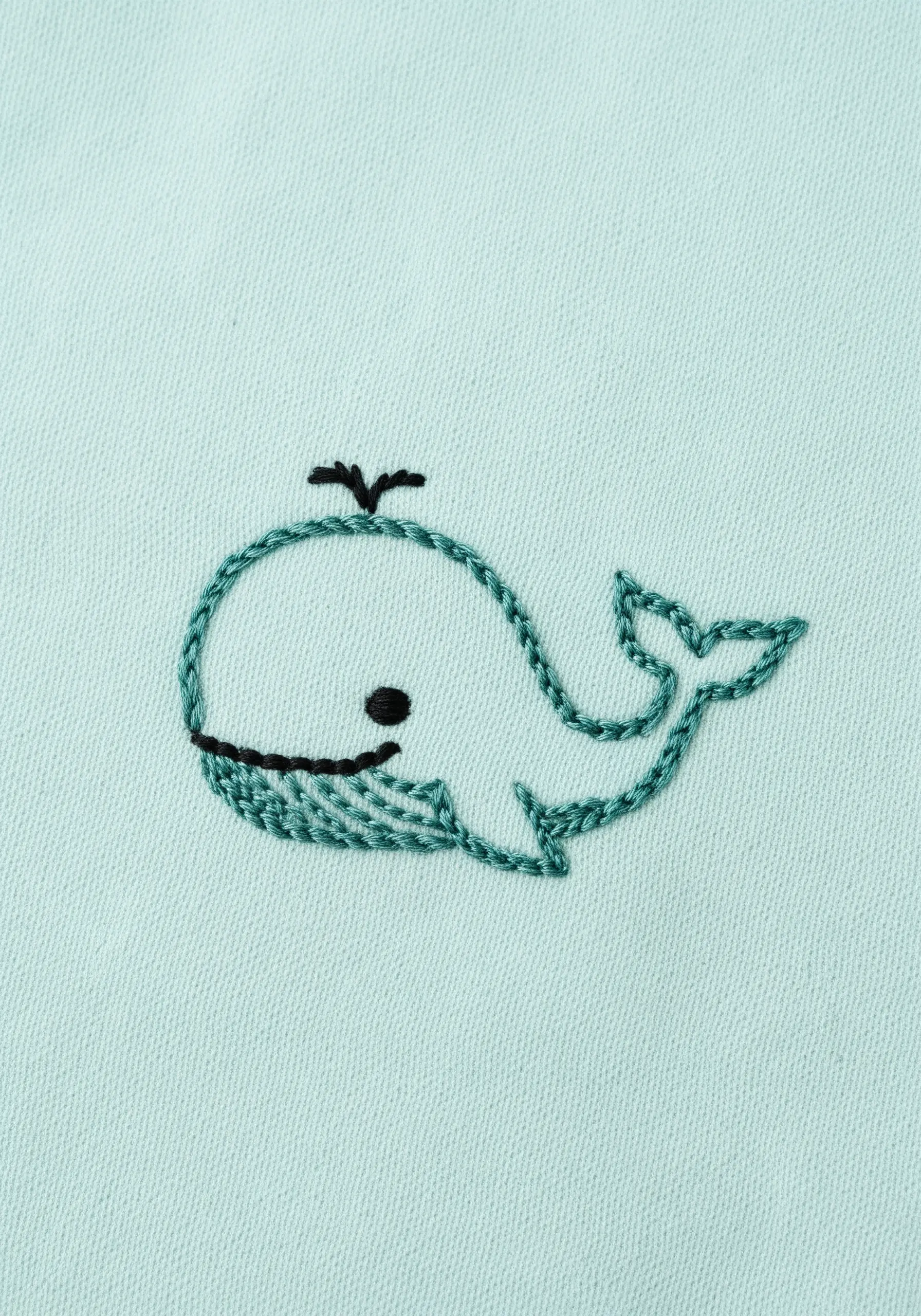 A simple outline of a whale embroidered in teal thread on mint fabric.