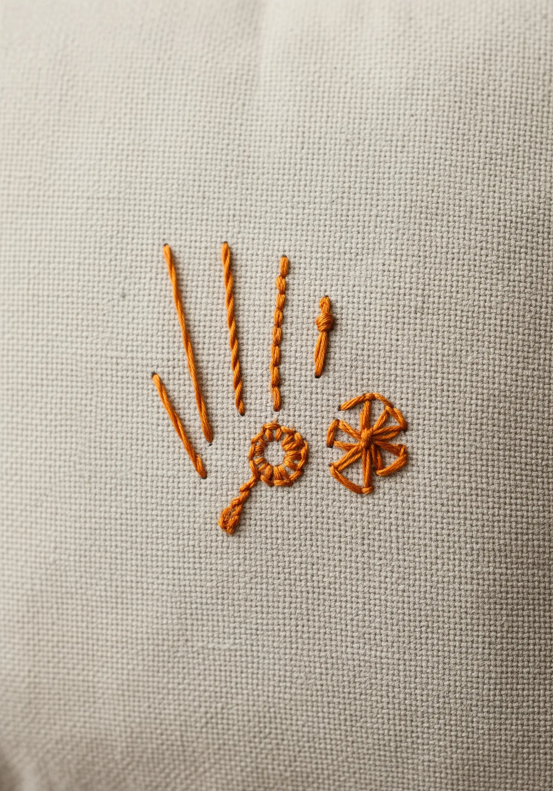 A small sampler of various embroidery stitches in shades of orange on a neutral fabric.