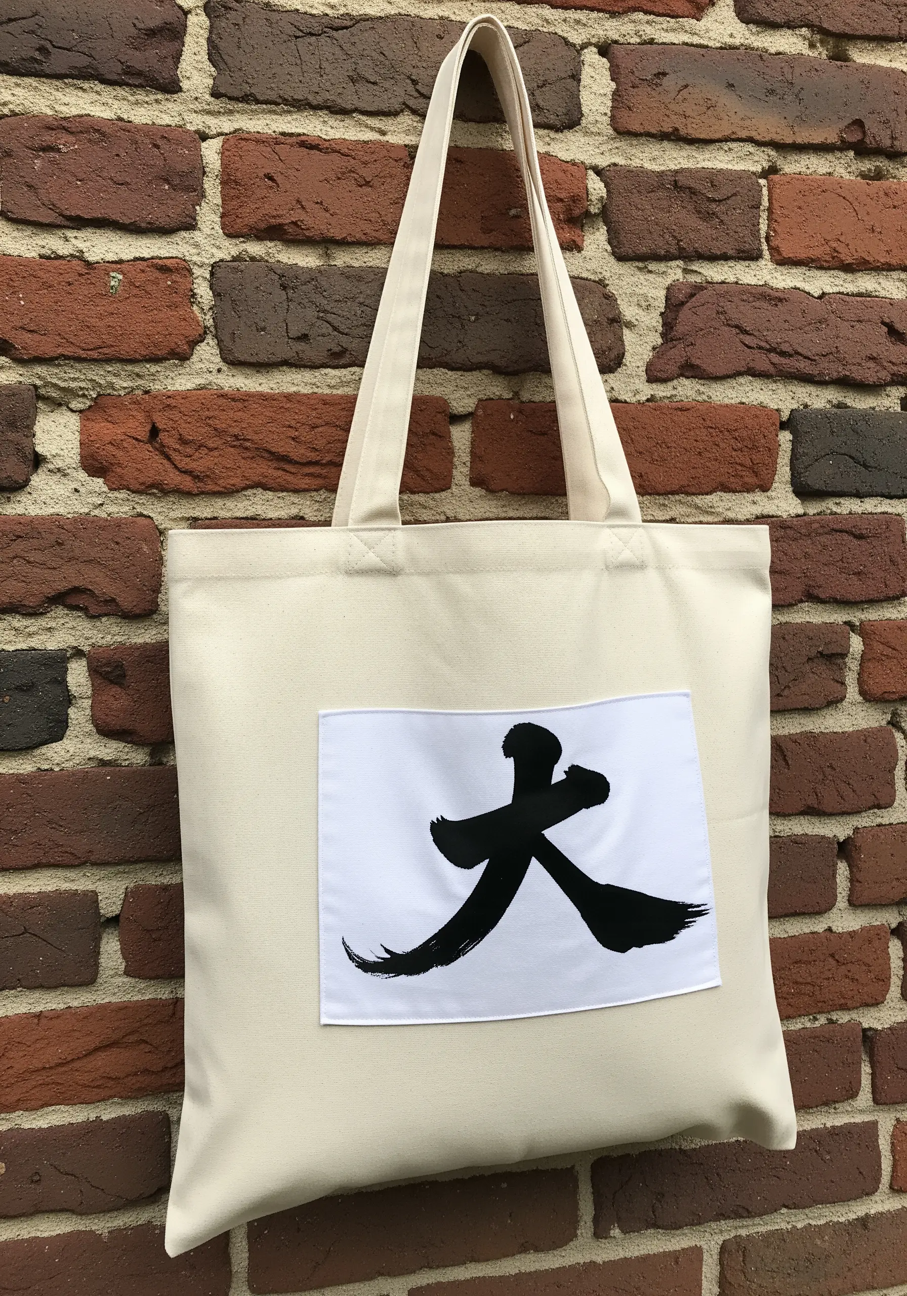 Black calligraphy brush stroke embroidered on a canvas tote bag