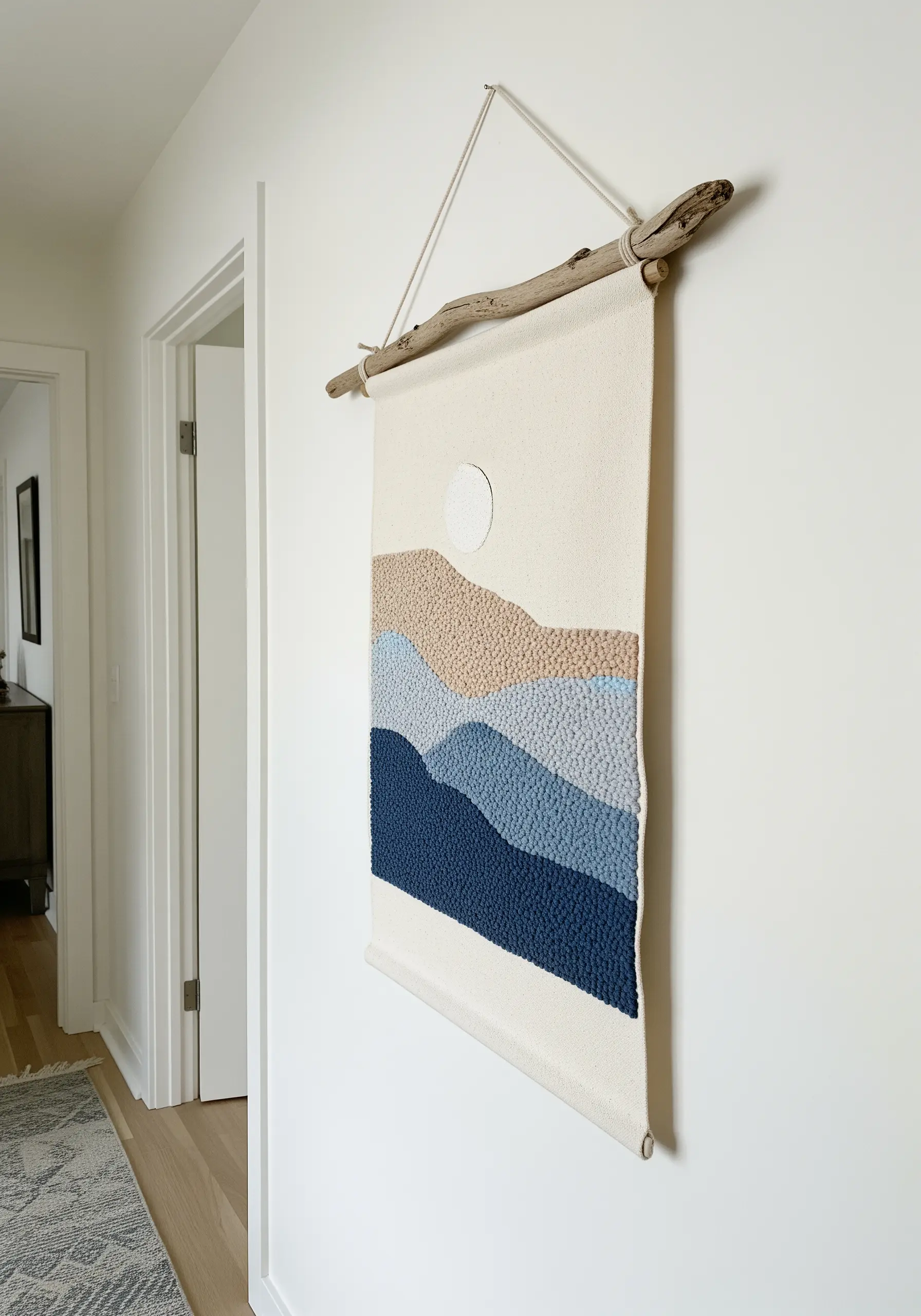A punch needle wall hanging of rolling hills in shades of blue, beige, and tan.