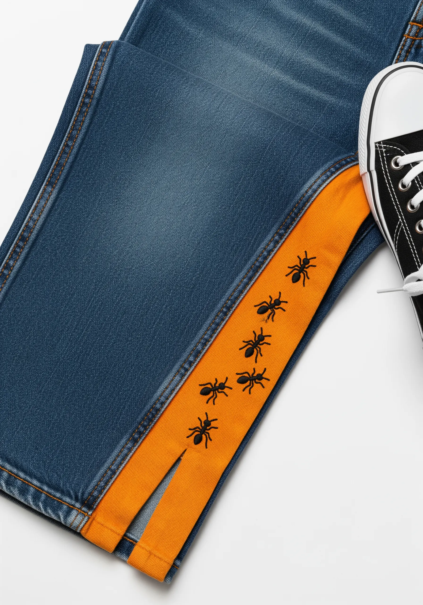 Tiny black ants embroidered in a line on an orange inner seam of blue jeans.