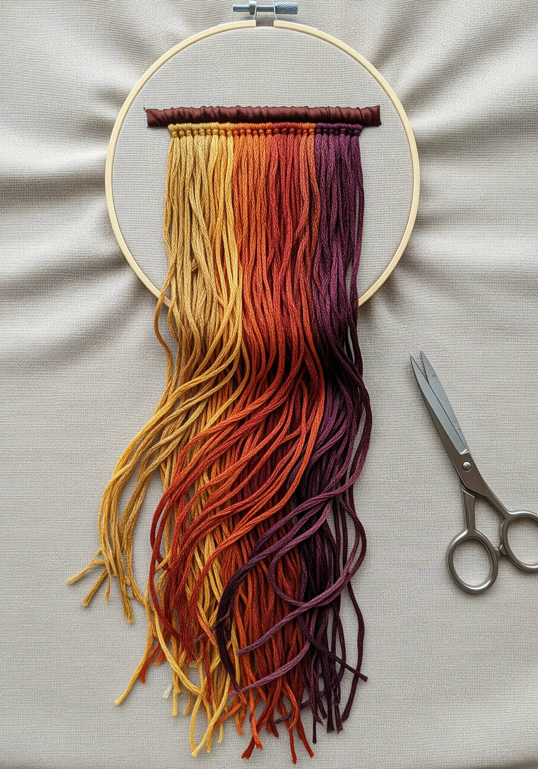 A waterfall of loose, untrimmed threads in a warm gradient hanging from a hoop.