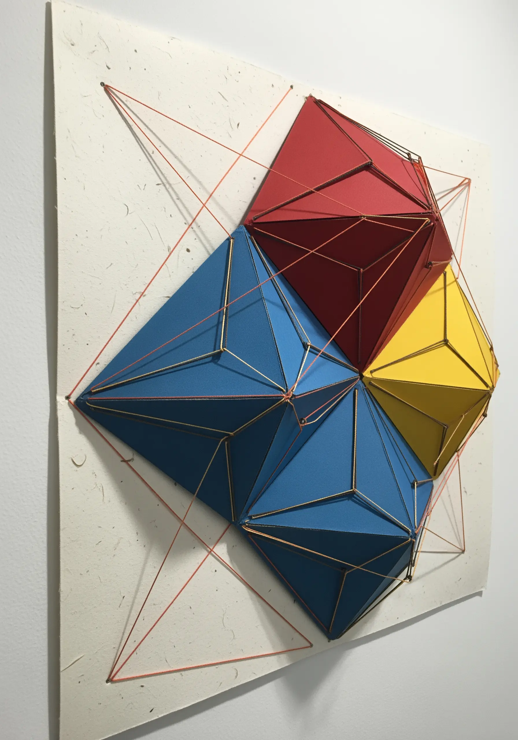 3D geometric paper sculptures connected and defined by taut red and gold thread.