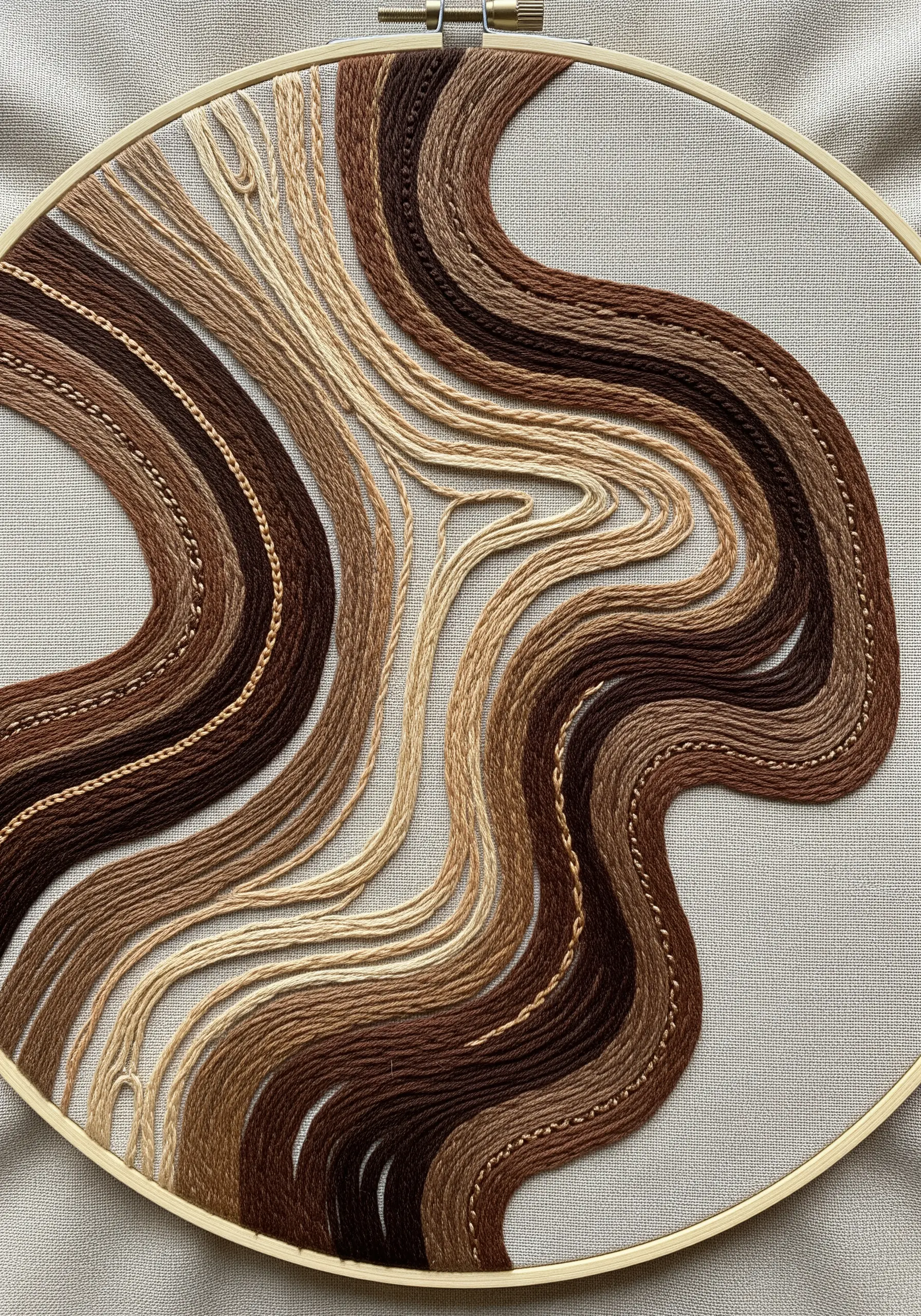 Abstract embroidery with flowing, couched lines in shades of brown, beige, and tan.
