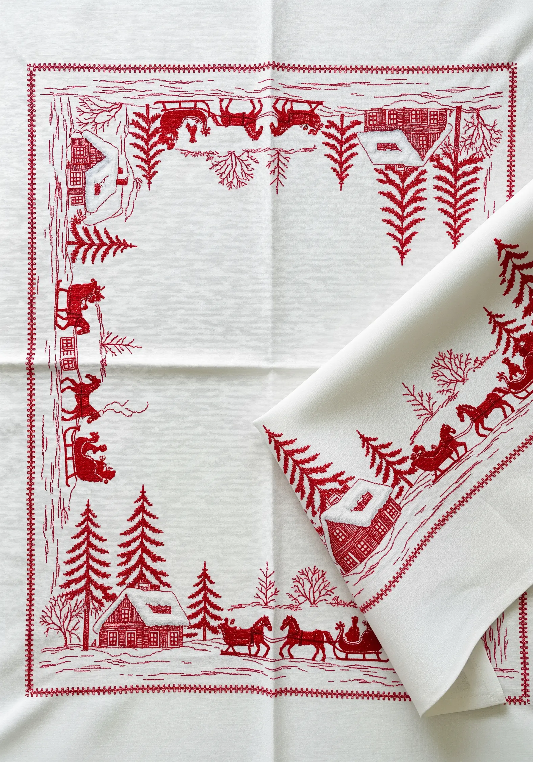 A traditional redwork embroidery winter scene bordering a white tablecloth.