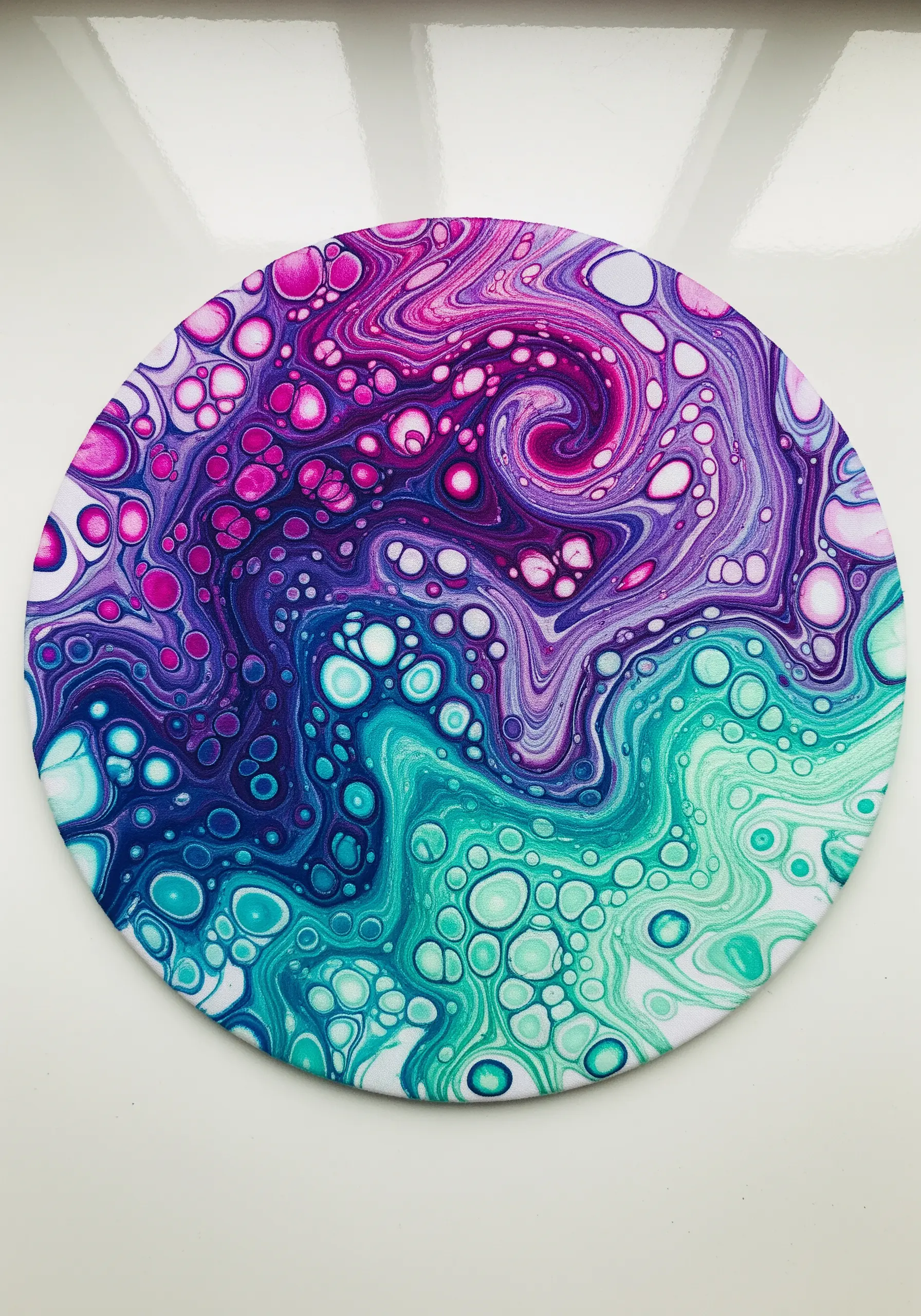 A circular canvas with a fluid paint-pour effect in purple, pink, and teal.