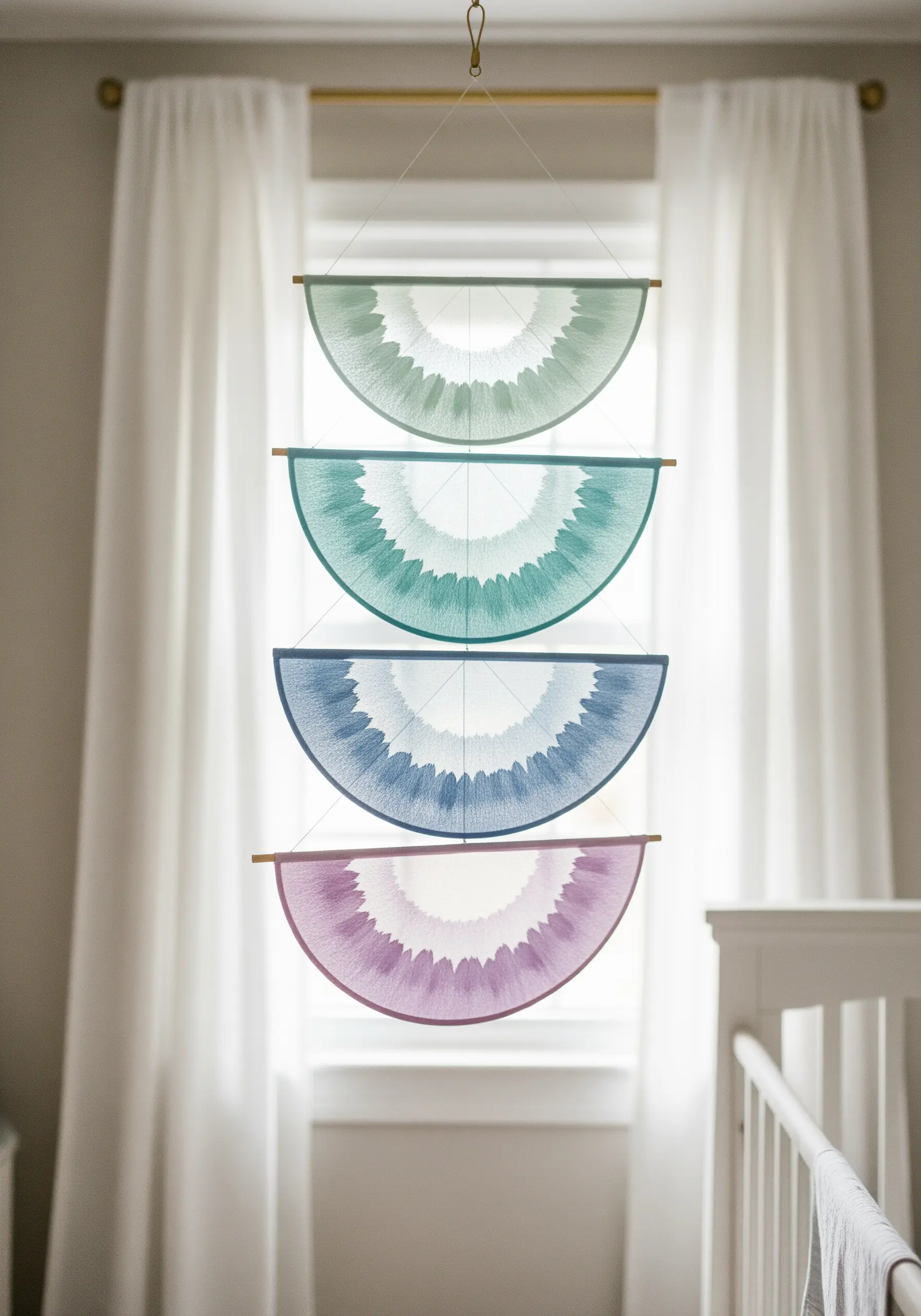 A mobile made of four embroidered semi-circles on sheer fabric in a pastel gradient.