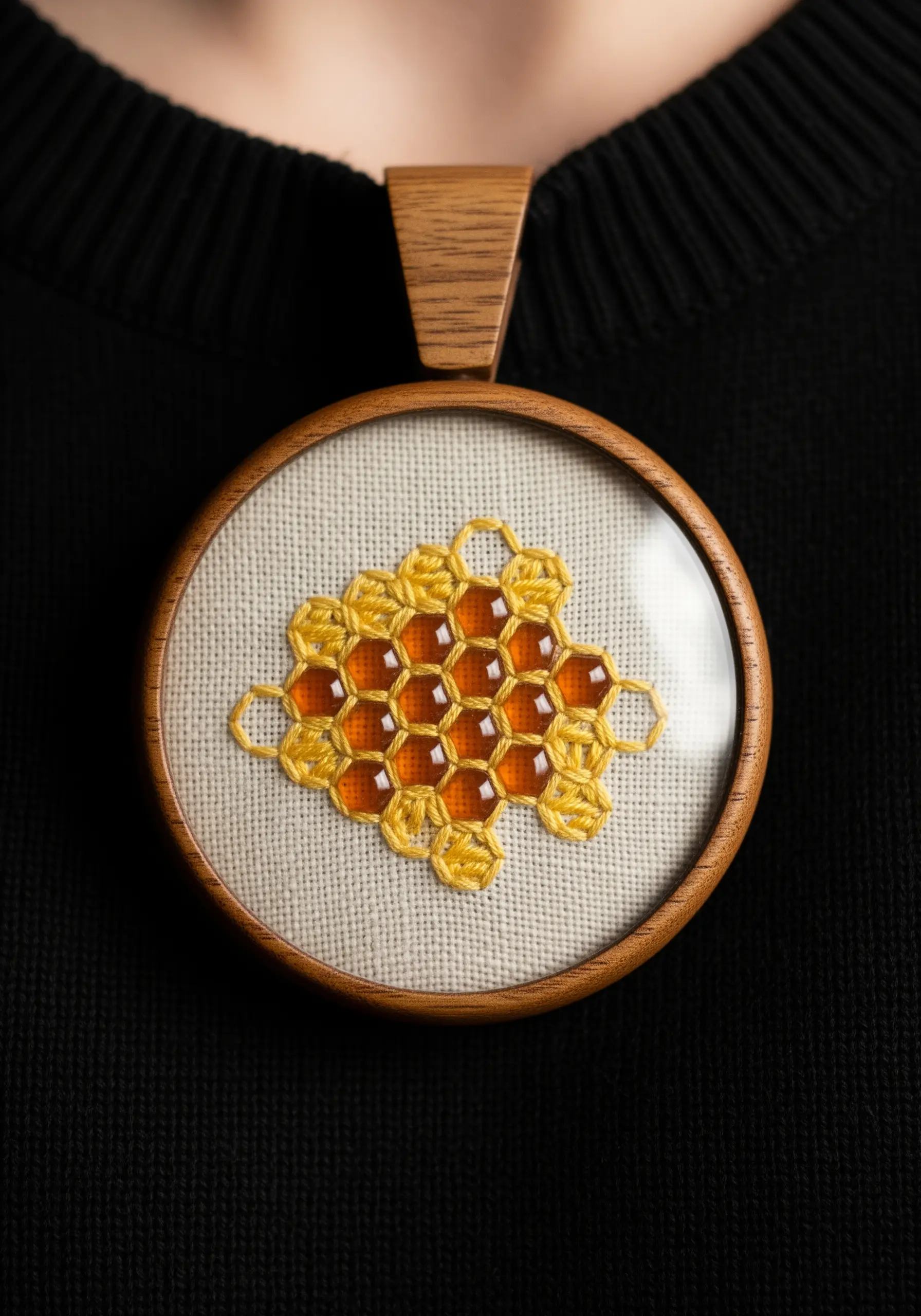An embroidered honeycomb pendant with resin-filled cells, worn on a black sweater.