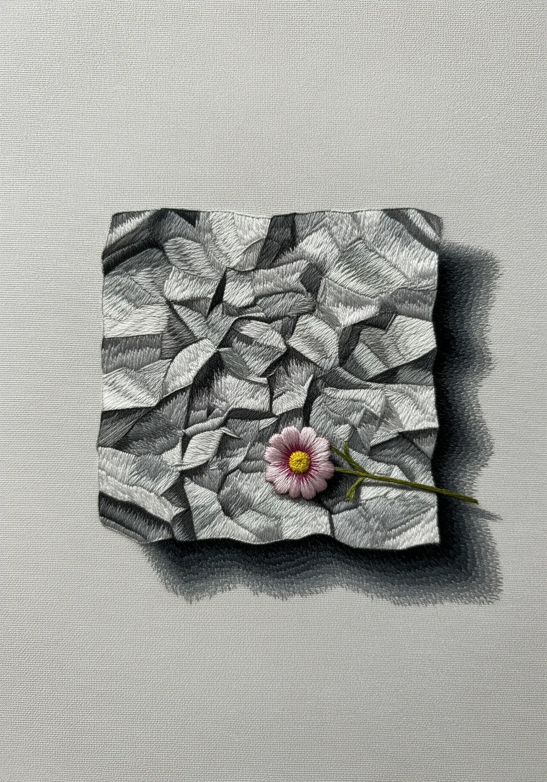 A hyper-realistic embroidery of a crumpled piece of paper with a single pink flower on top.