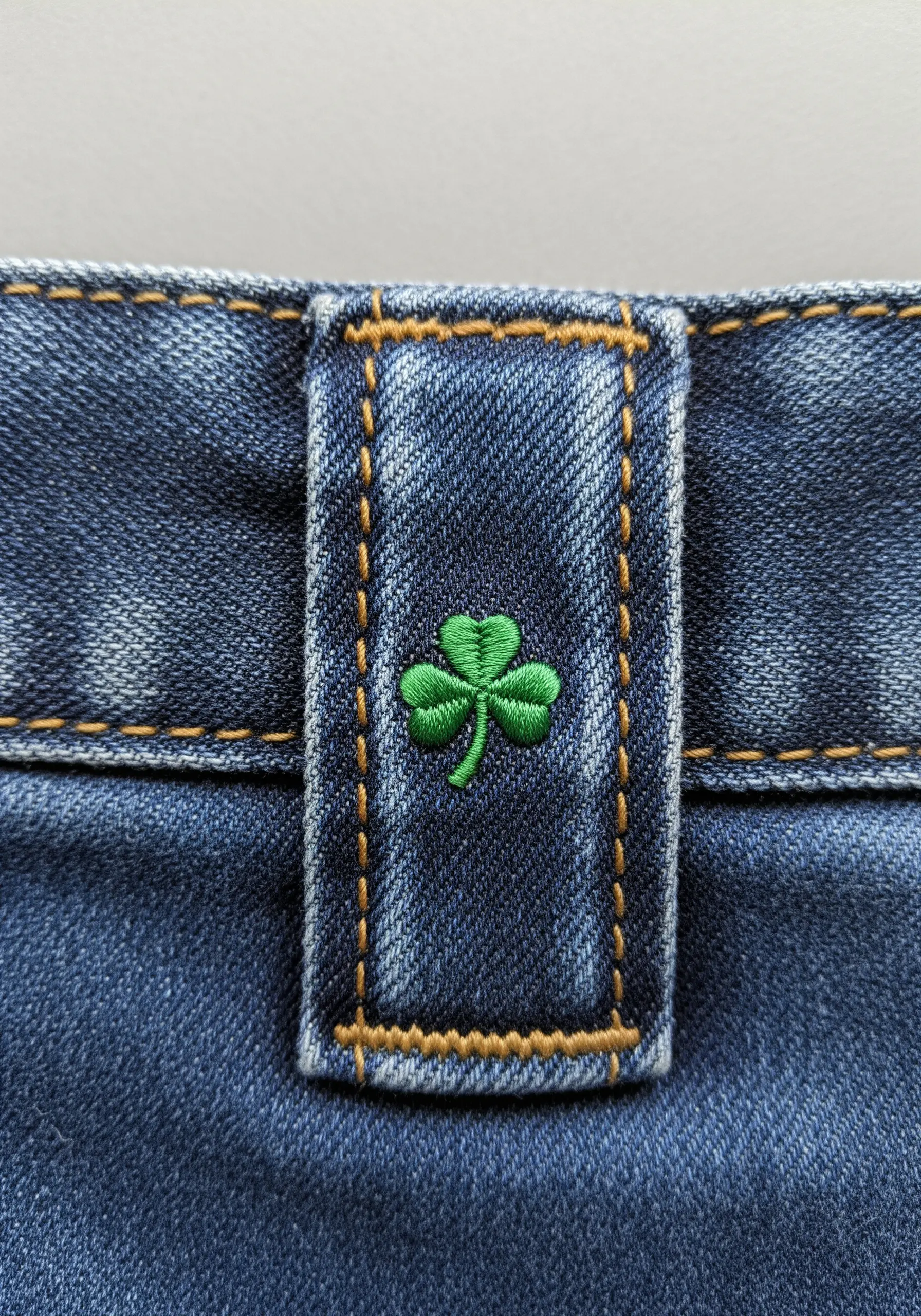 A tiny, bright green shamrock embroidered on the belt loop of a pair of blue jeans.