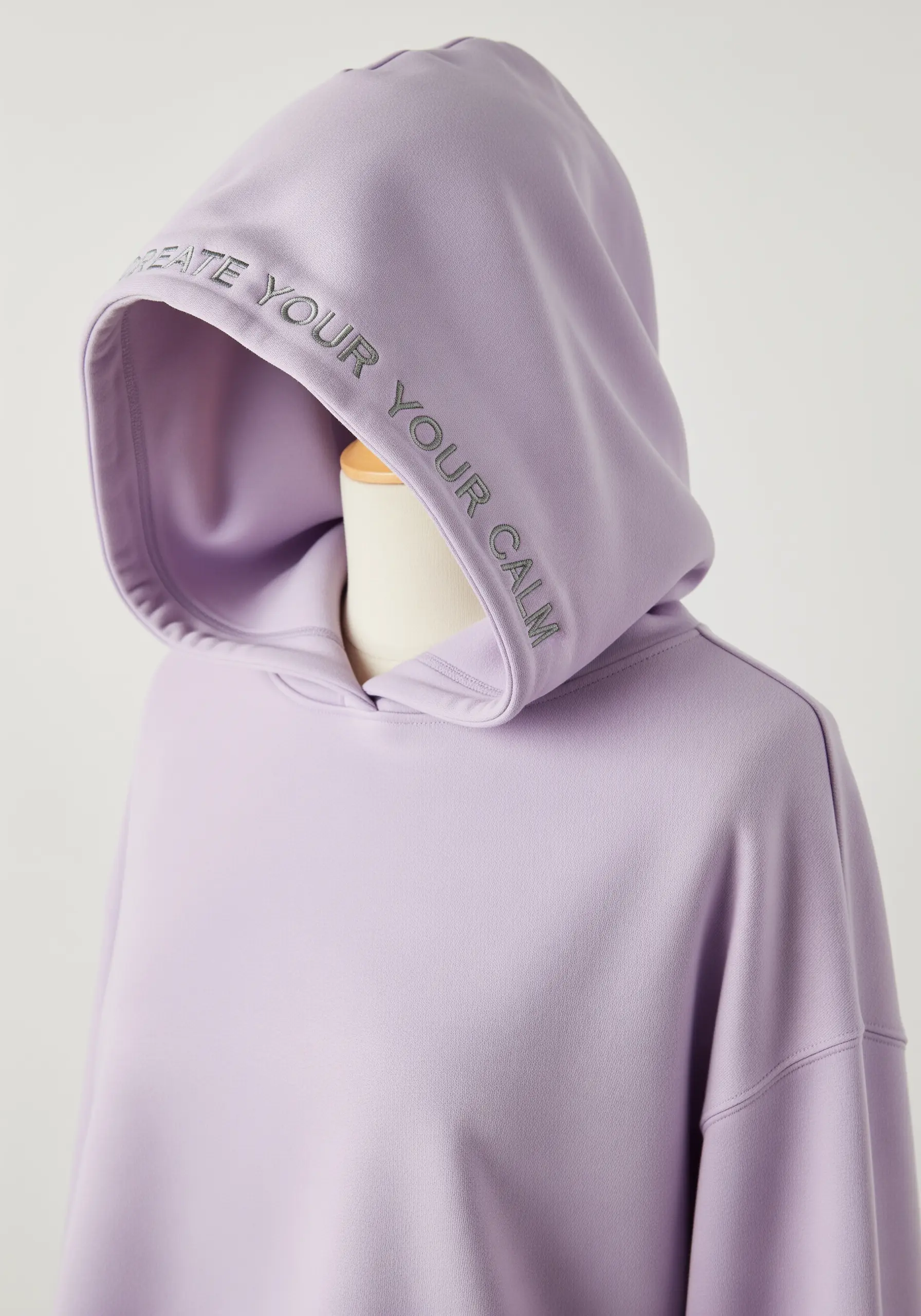 “CREATE YOUR YOUR CALM” embroidered in grey along the edge of a lavender hoodie.