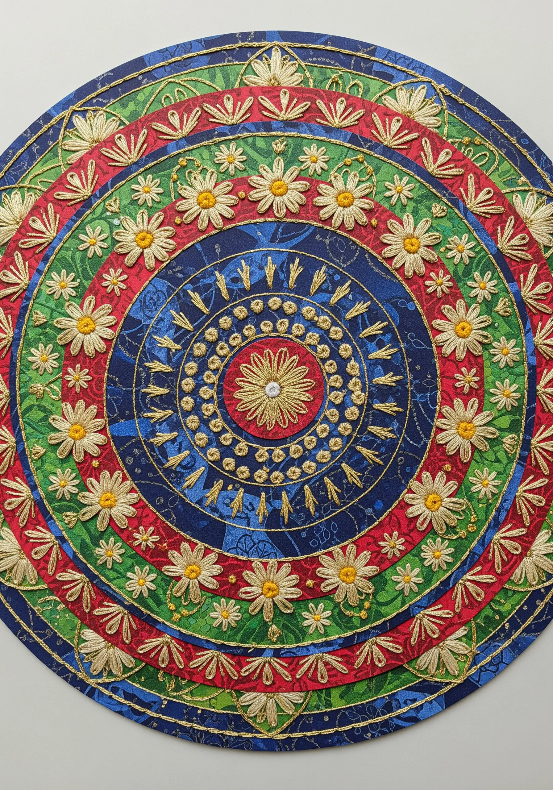 A colorful mandala collage on patterned paper, unified with gold thread embroidery details.