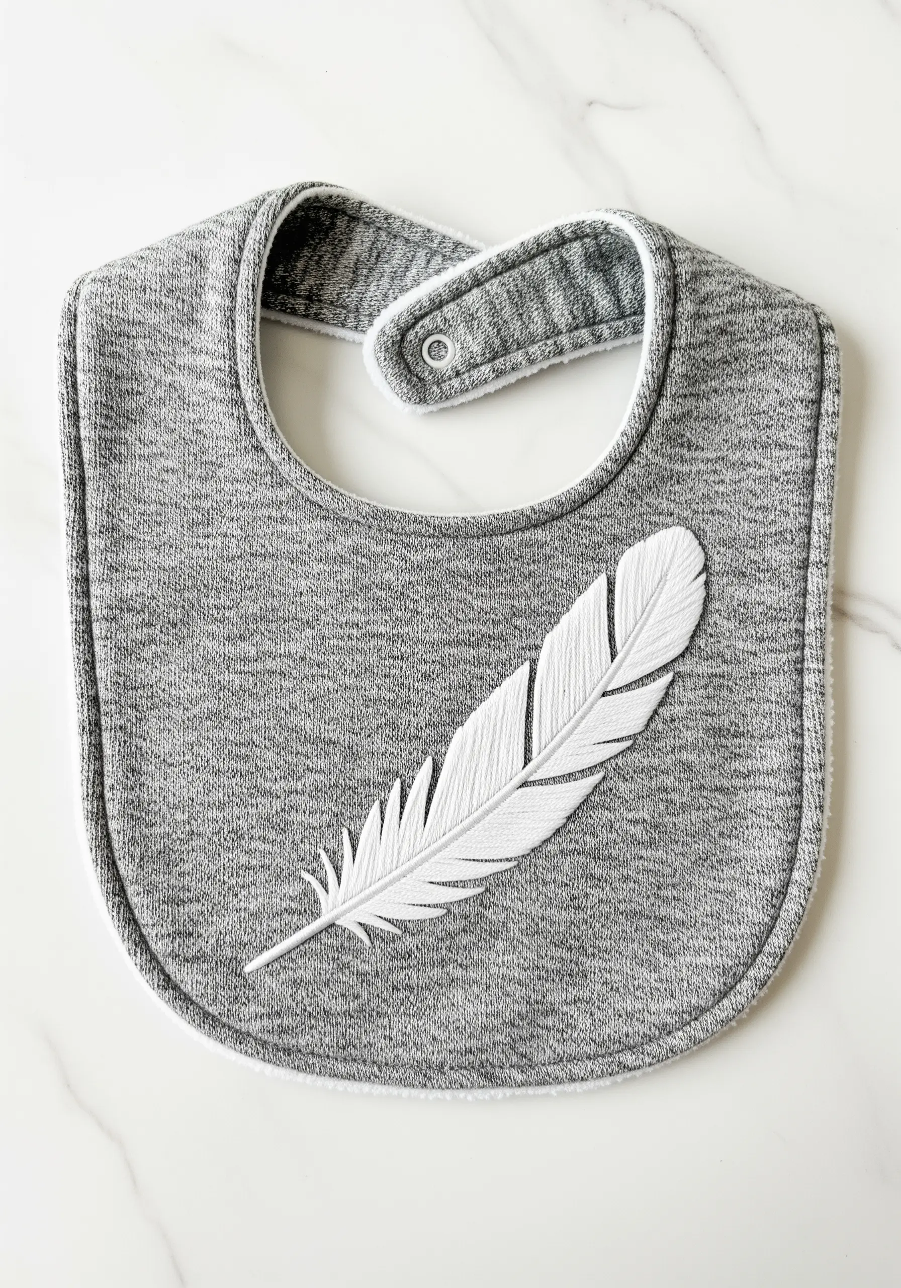 A large white feather embroidered on a grey bib using directional stitches for texture.