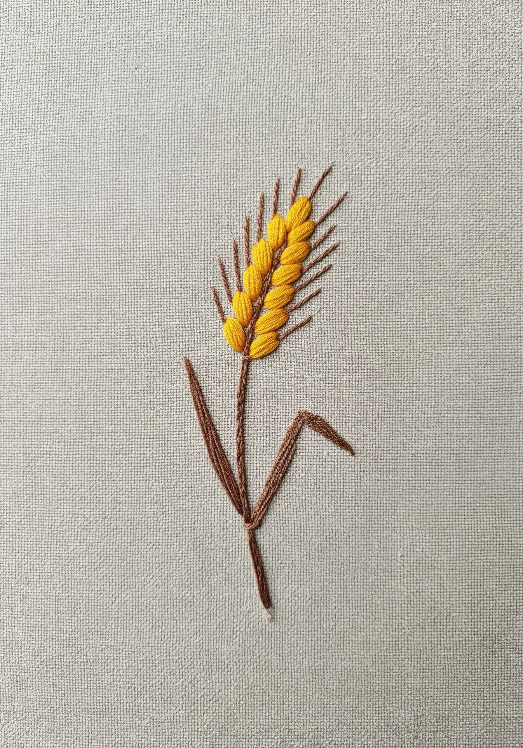 A single stalk of wheat embroidered with yellow fishbone stitch grains and a brown stem.
