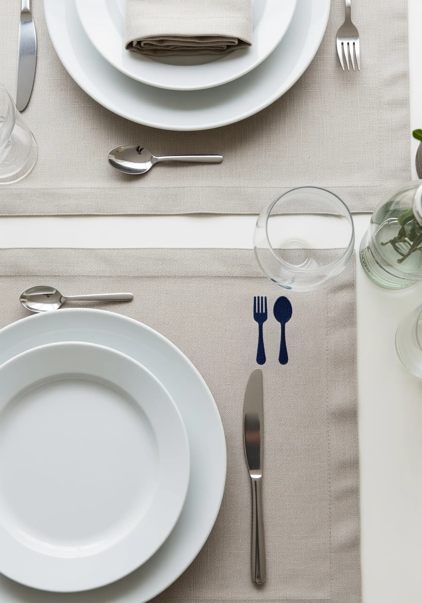 A dark blue embroidered silhouette of a fork and spoon on a neutral placemat.