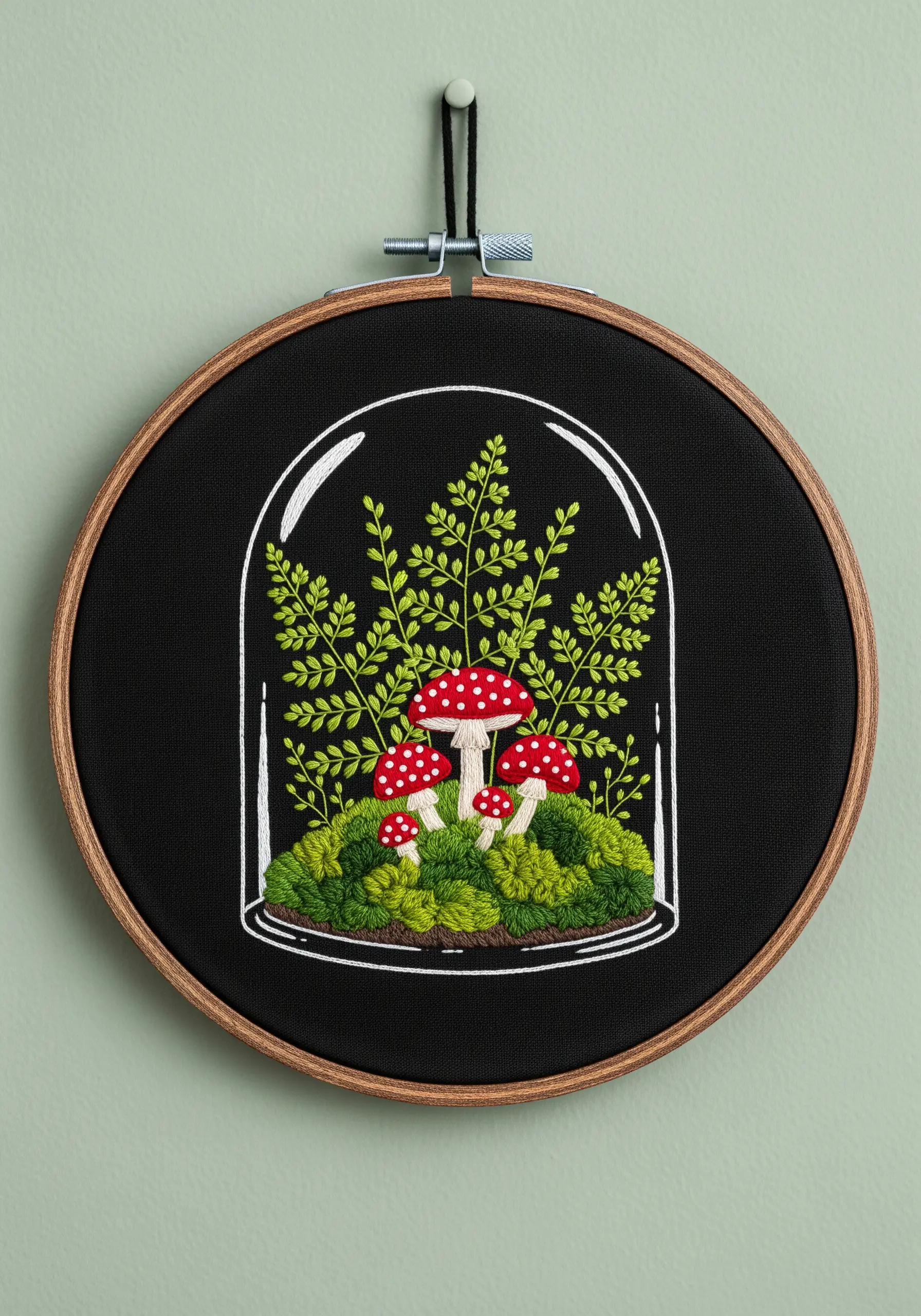 Embroidered mushrooms and ferns under a glass cloche on black fabric