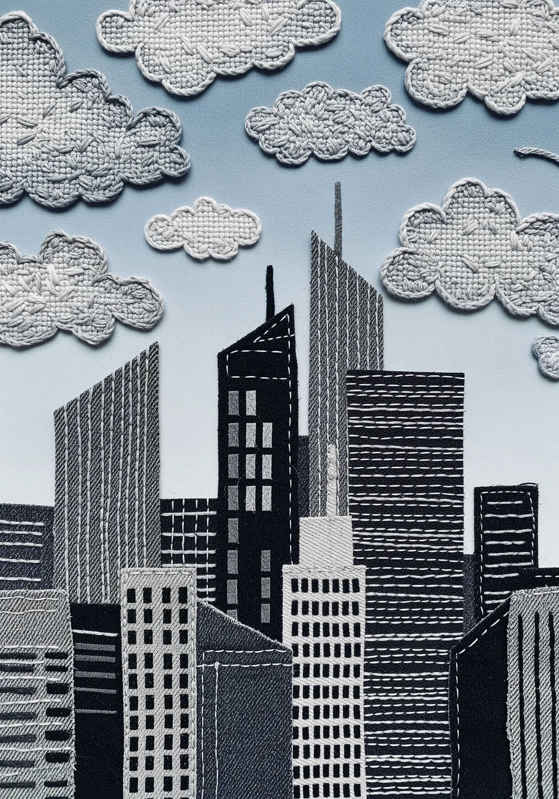 A fabric collage cityscape with linear stitching to create window and building details.