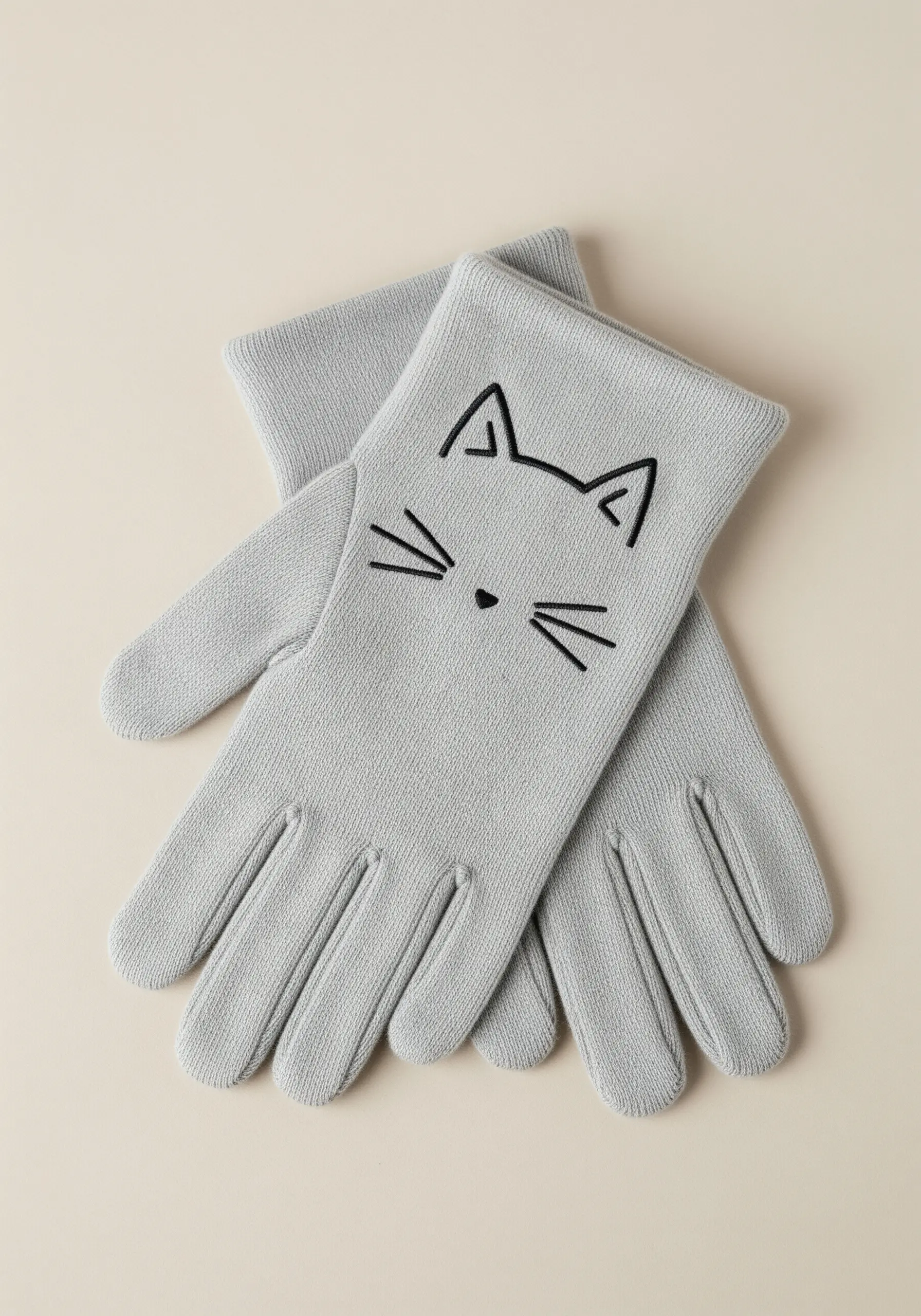 A minimalist cat face embroidered with black thread on a pair of light gray knit gloves.
