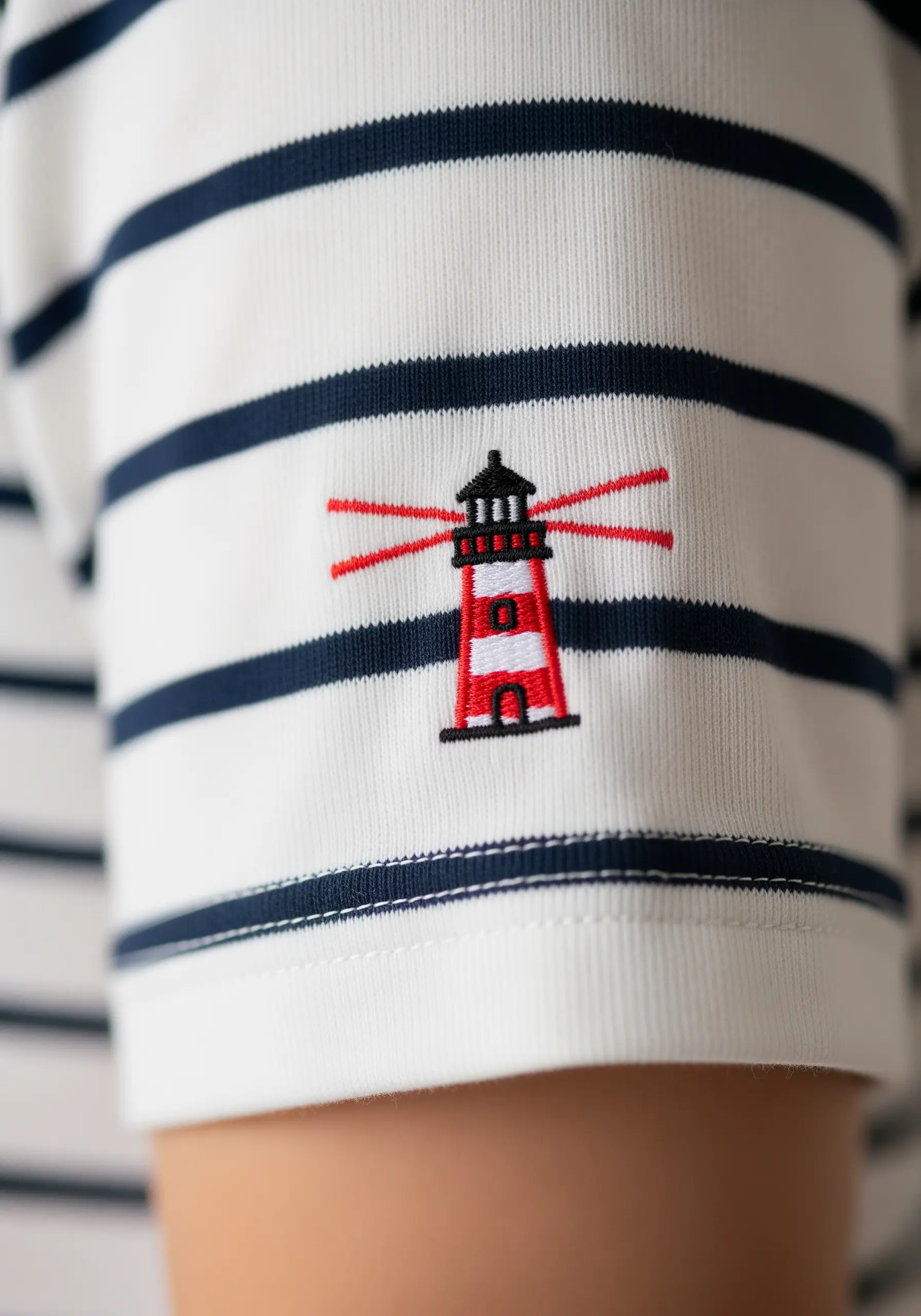 A small red and black lighthouse embroidered on the sleeve of a striped shirt.