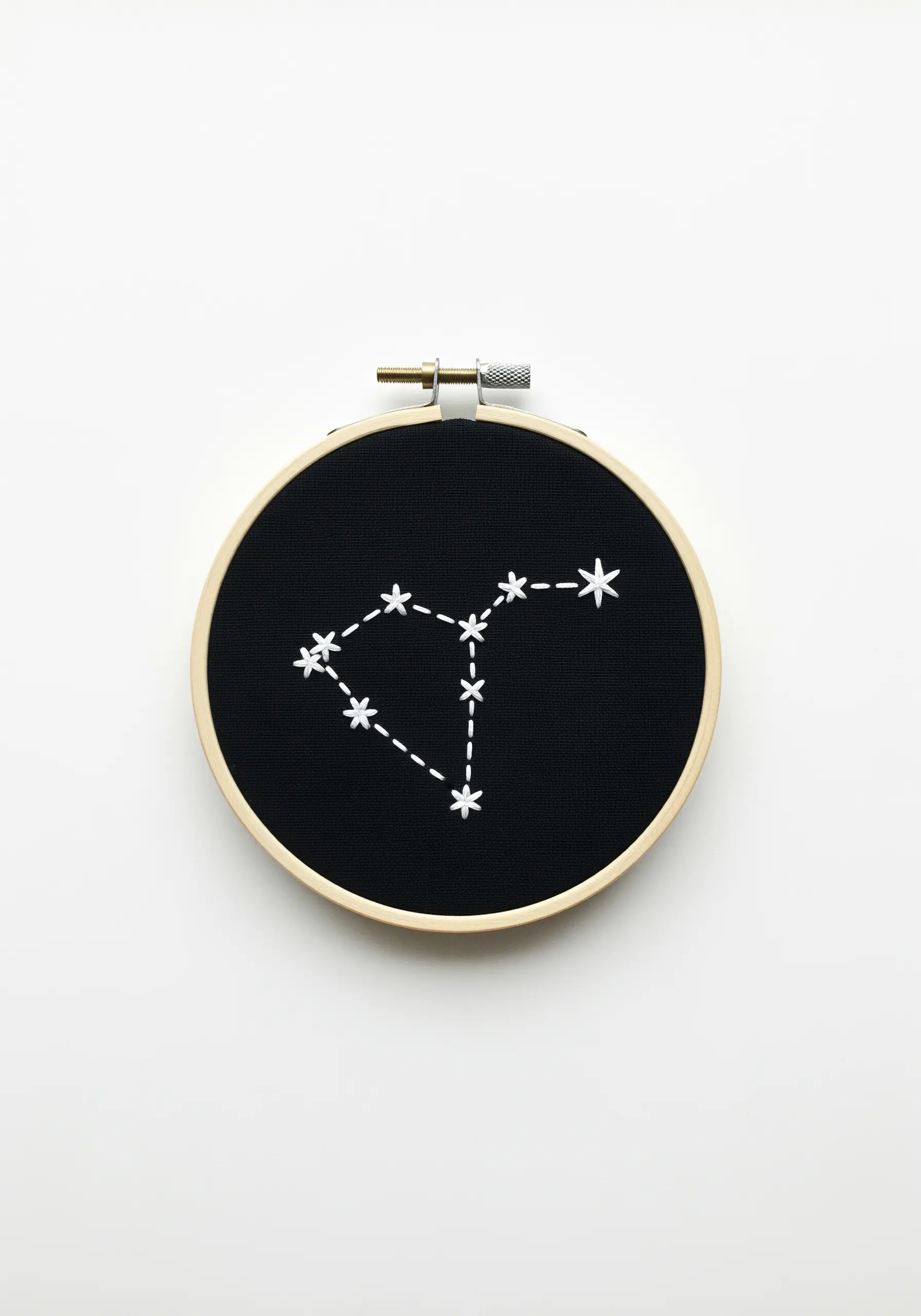 A constellation stitched in white thread on black fabric inside an embroidery hoop.