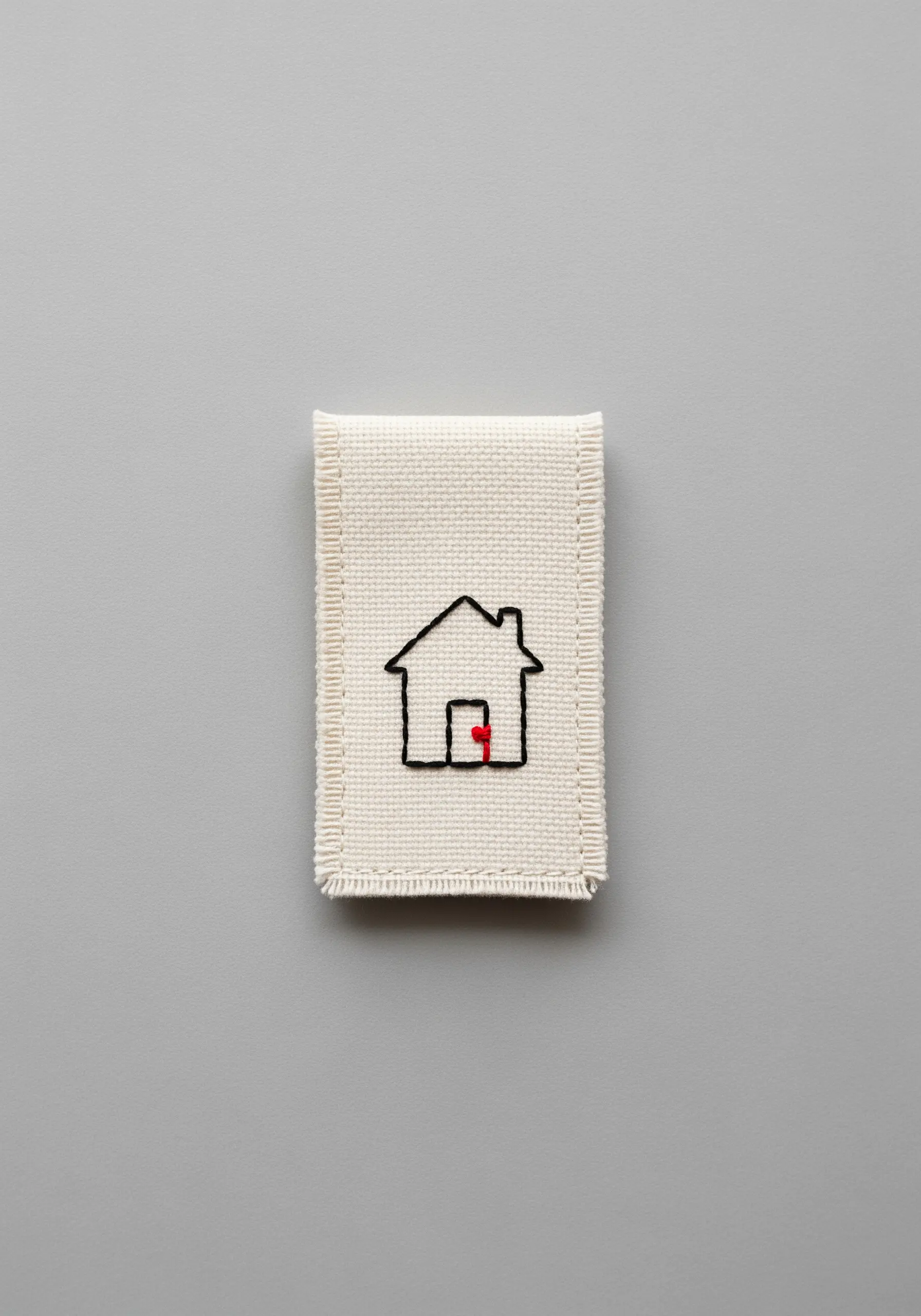 A minimalist black outline of a house with a small red door, stitched on Aida cloth.