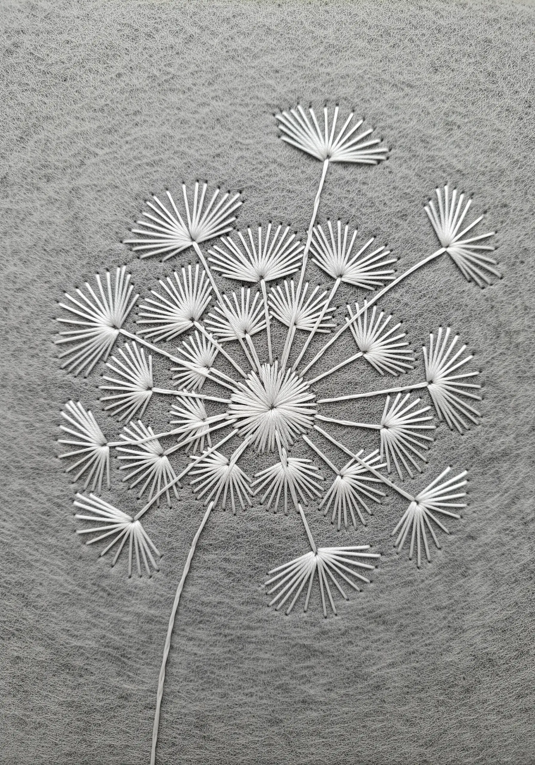 A stylized dandelion head embroidered with radiating white straight stitches on gray felt.