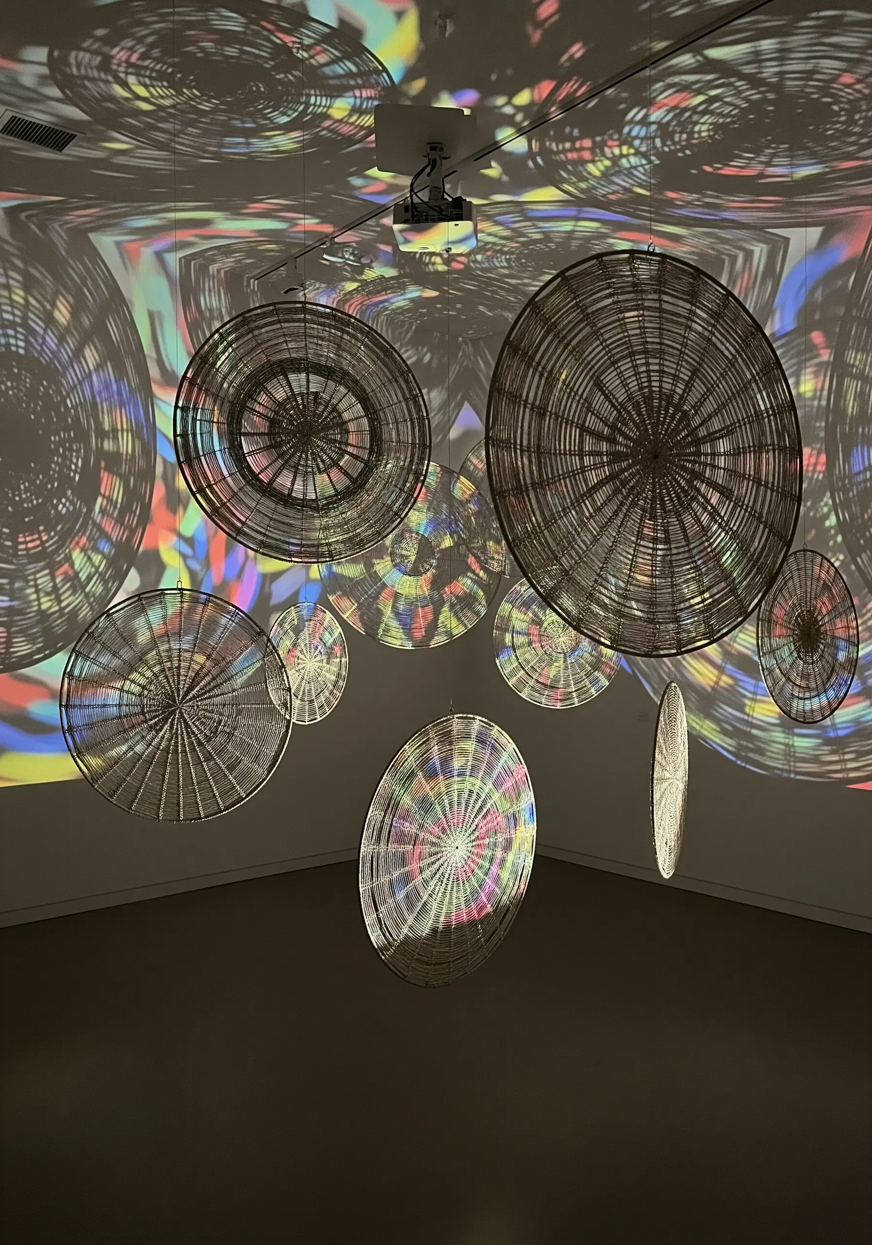 A neutral-colored, highly textured embroidery piece with colorful light projected onto it.