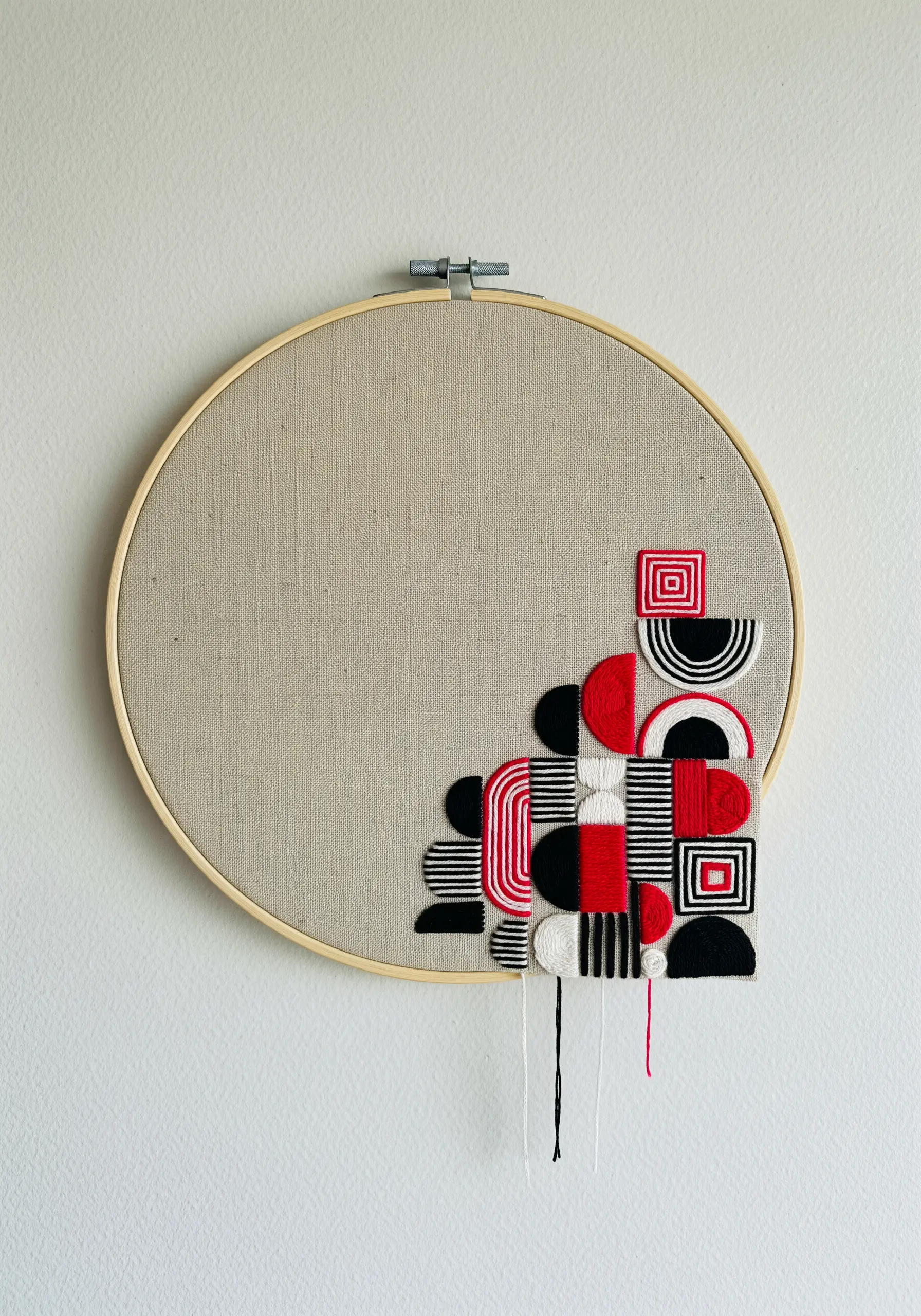 Asymmetrical geometric embroidery in red, black, and white in the corner of a hoop.