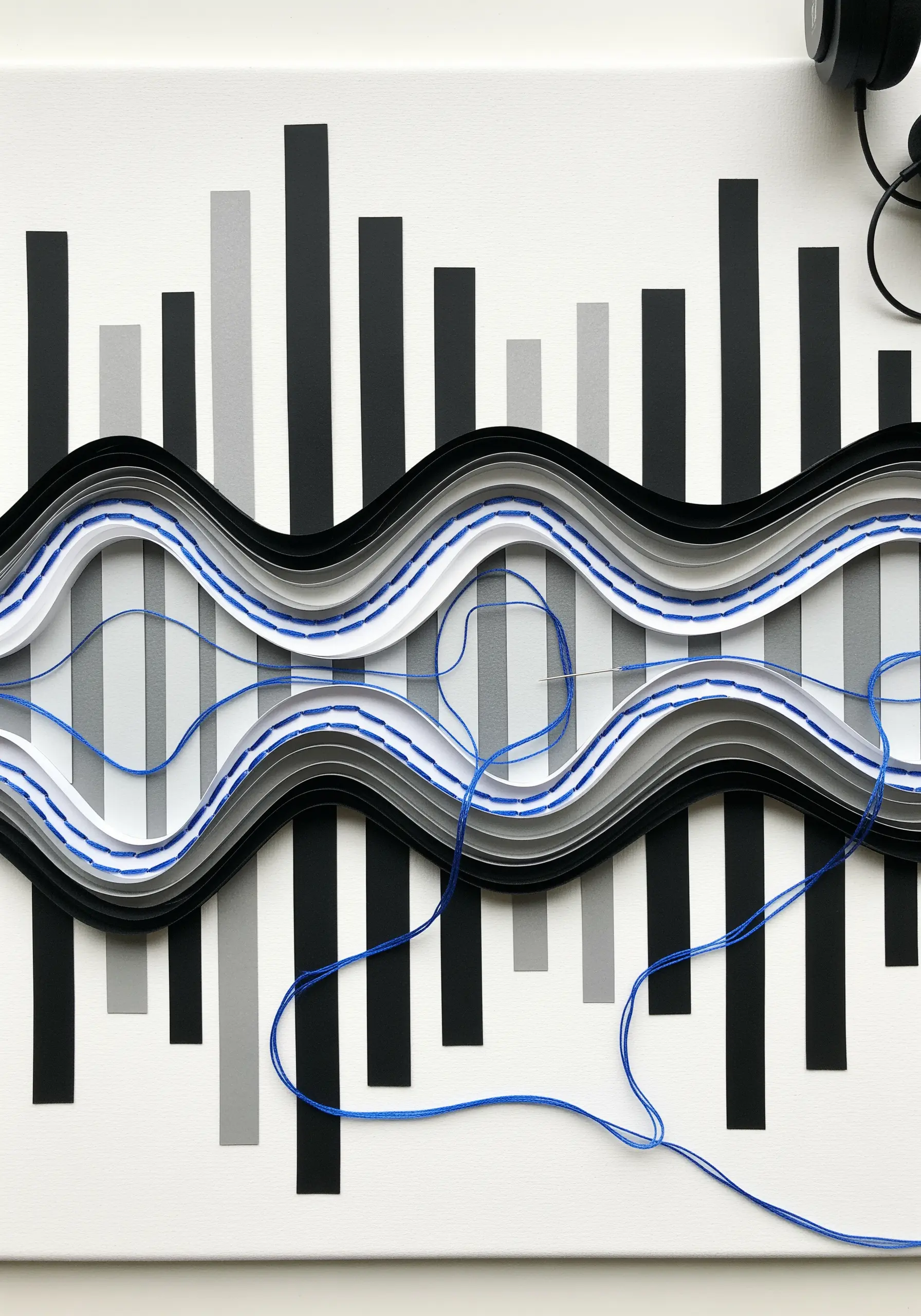 An abstract sound wave sculpture made from layered paper strips and blue thread.