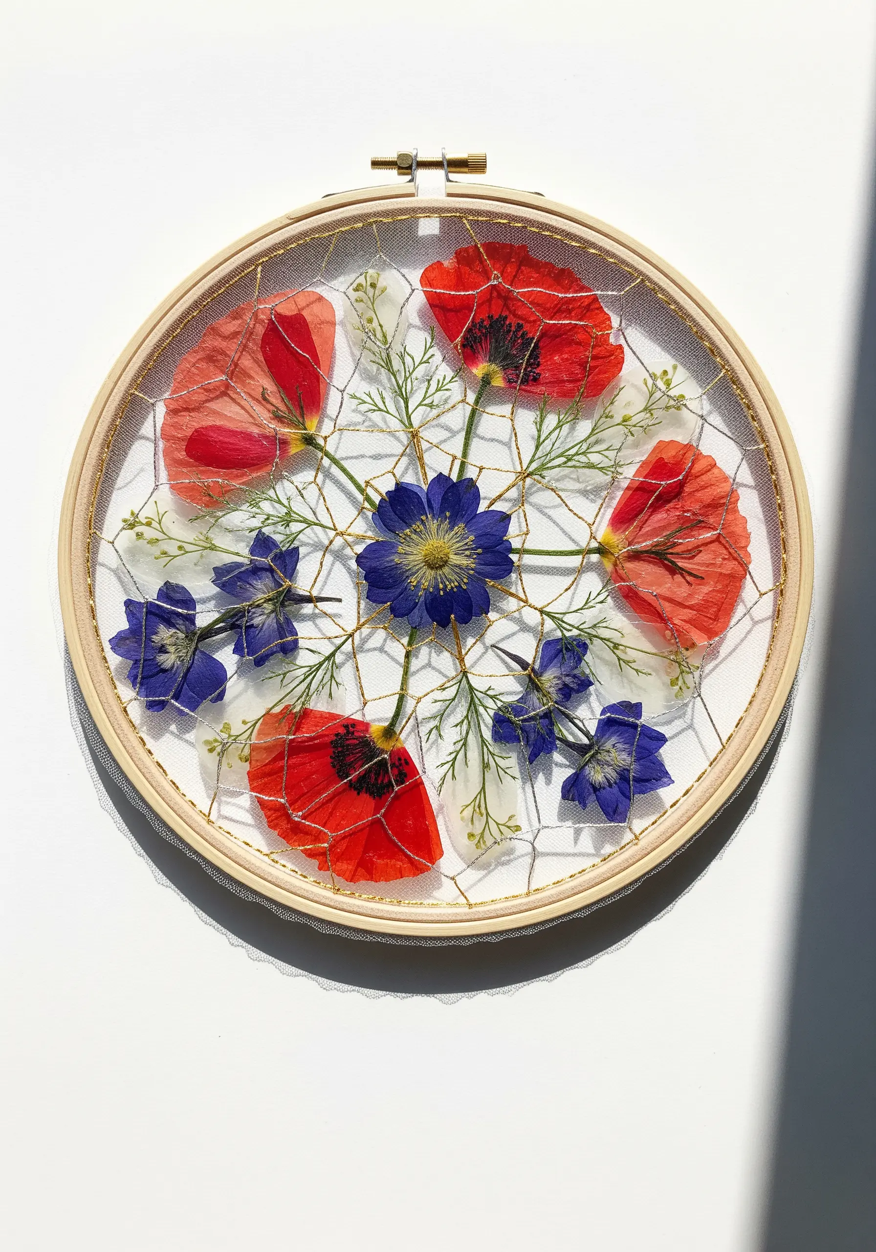 Pressed poppies and delphiniums woven into a gold thread web on a sheer tulle background.