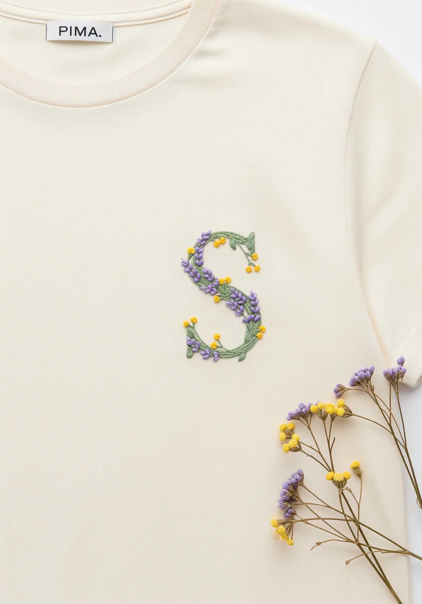 Letter 'S' embroidered with delicate purple lavender stems and tiny yellow floral knots.