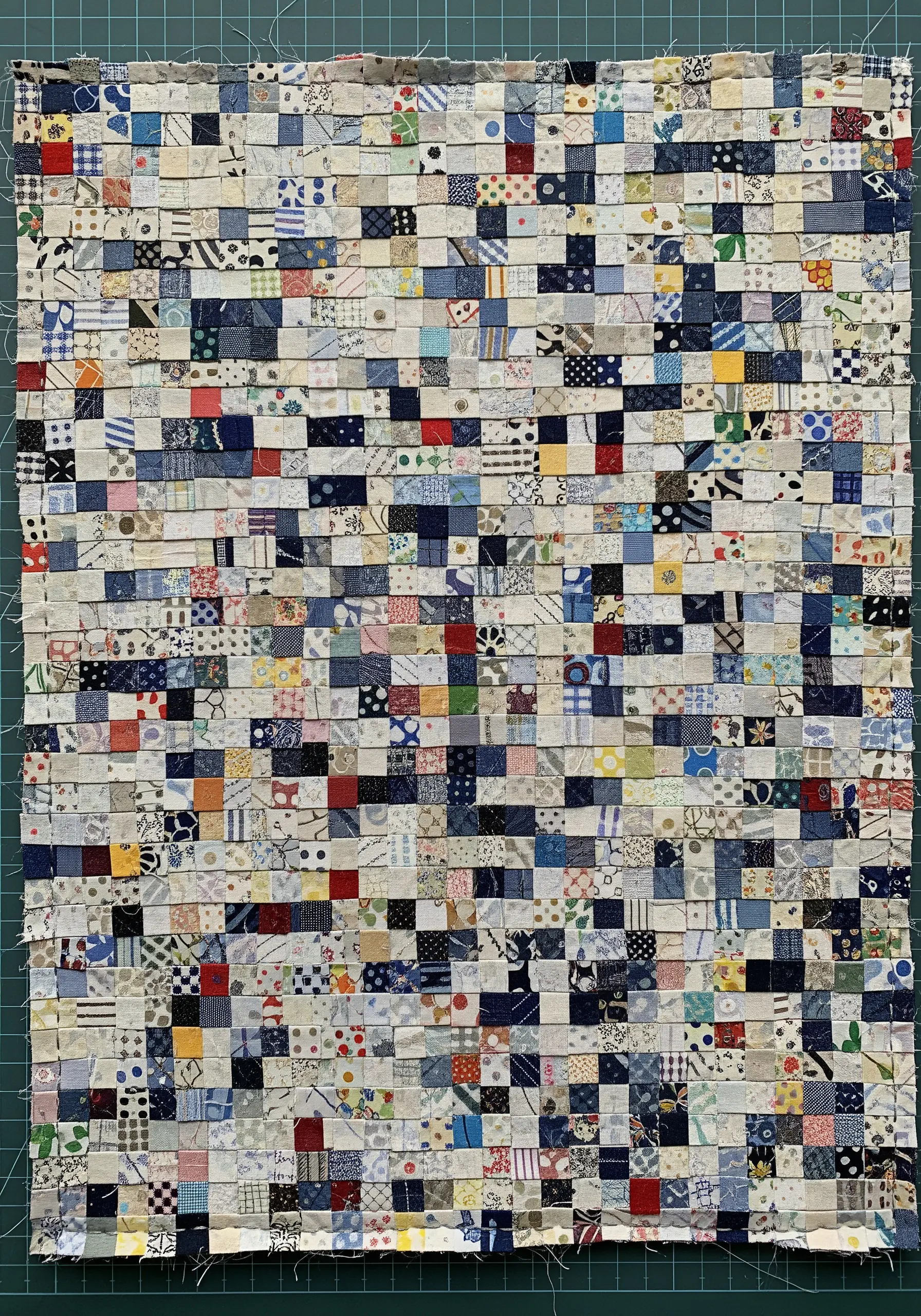 A dense, colorful fabric collage created by weaving tiny, narrow strips of patterned fabric together.