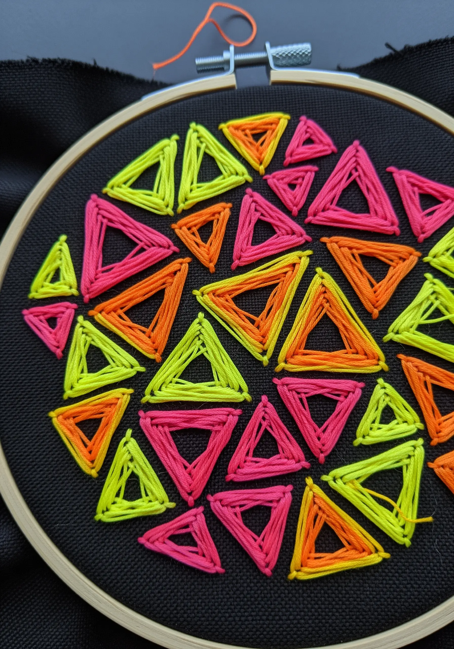 Woven neon triangles in yellow, pink, and orange stitched on black fabric in a hoop.