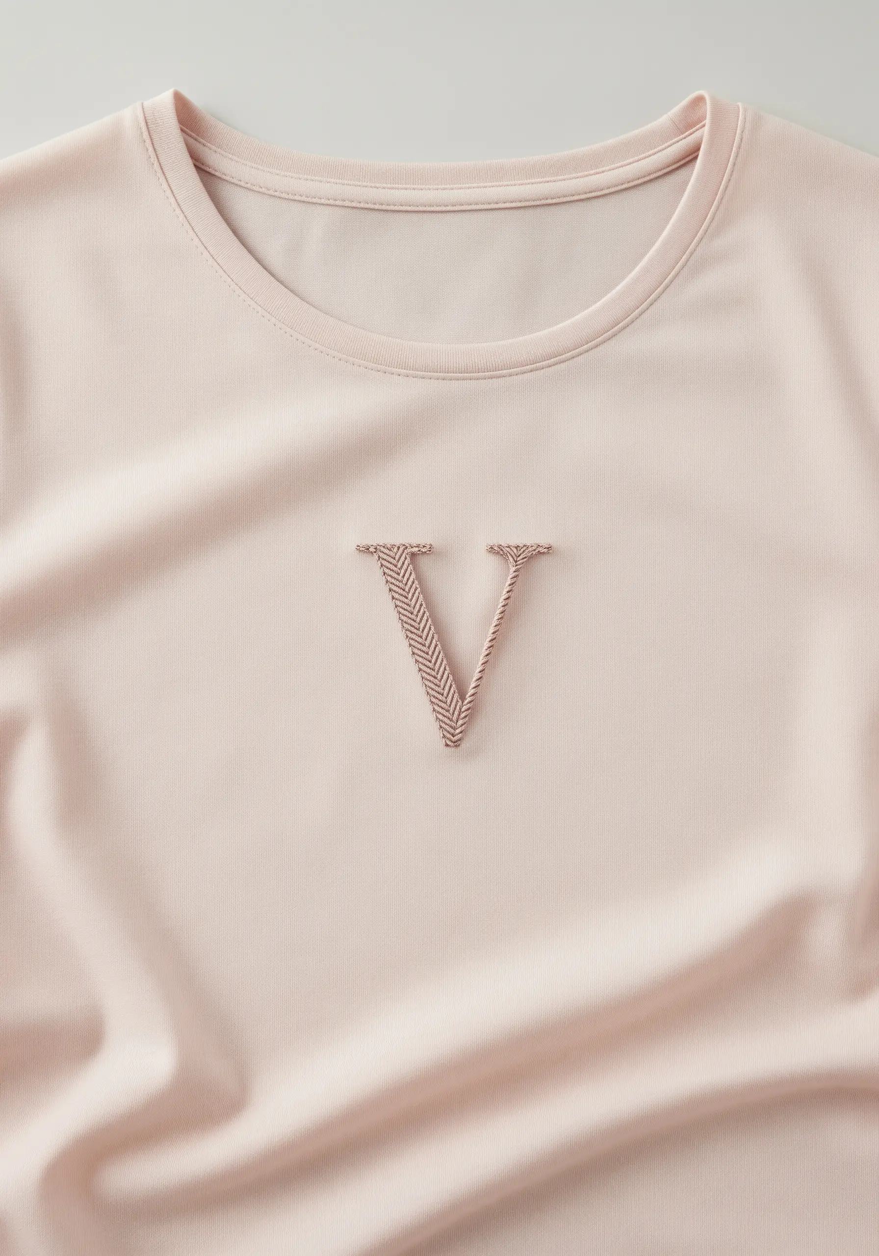 A close-up of the letter 'V' filled with a neat, textured herringbone stitch in a rose gold thread.