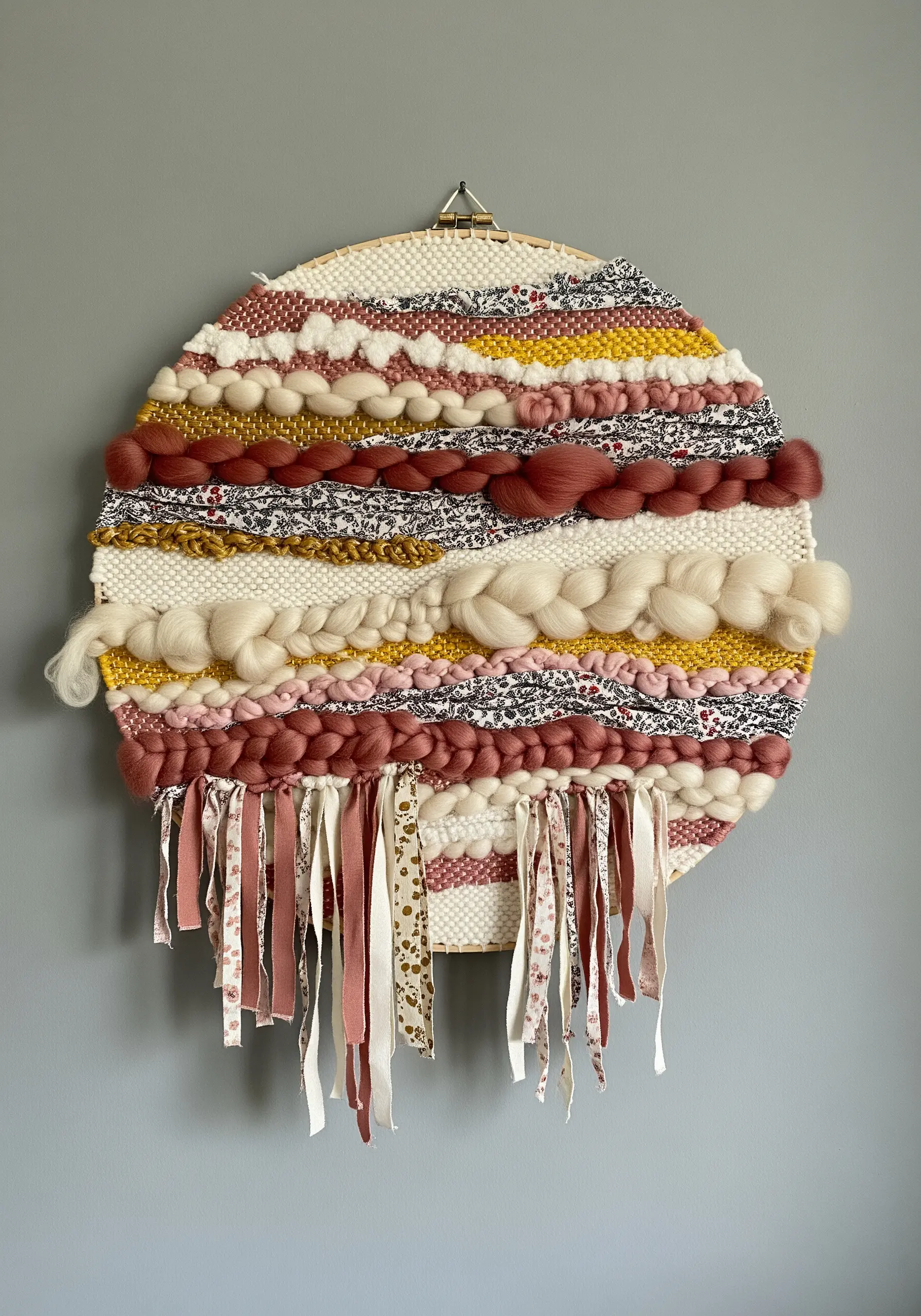 A circular woven wall hanging in an embroidery hoop with various yarns and fabrics.