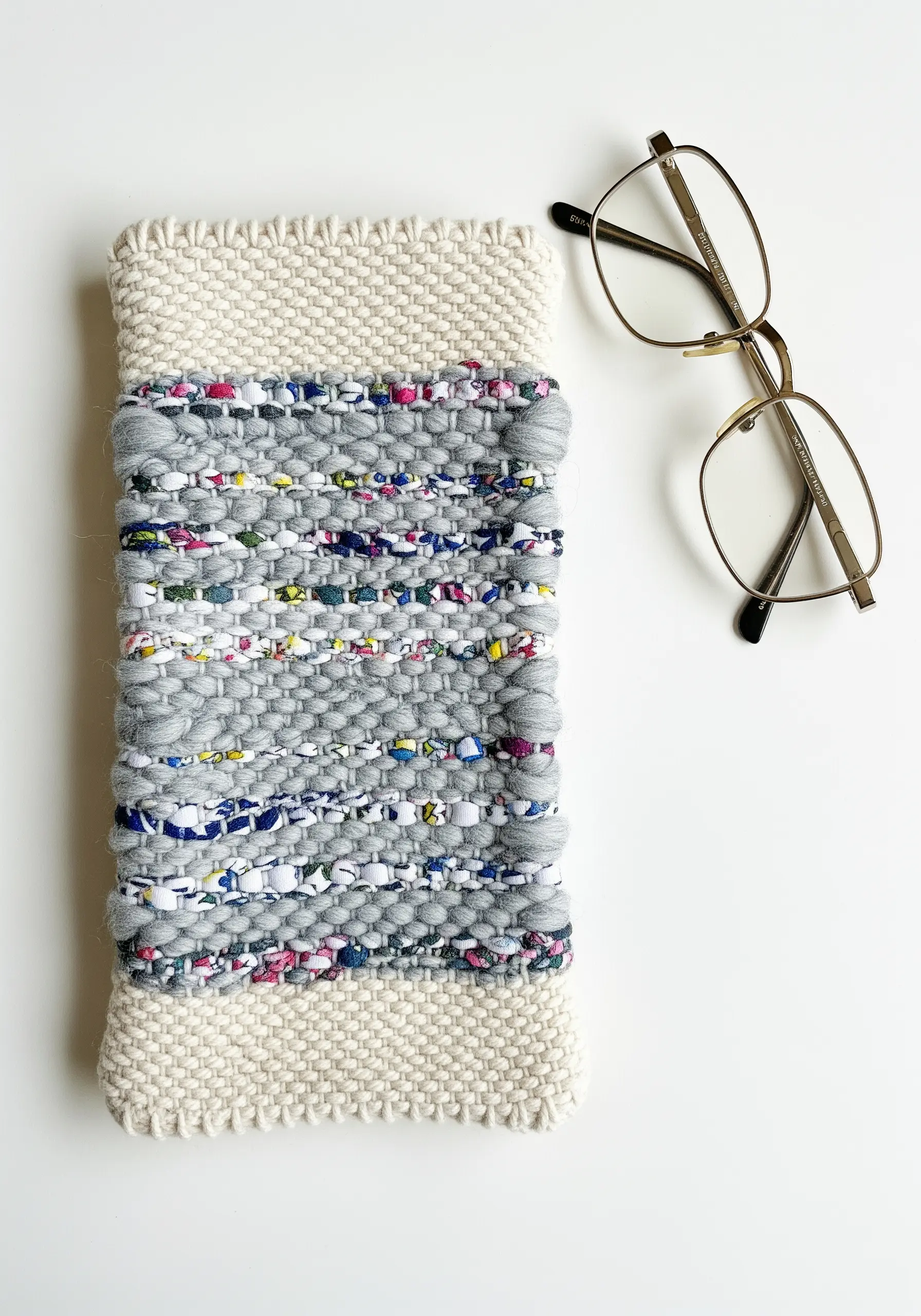 A woven glasses case made with neutral grey and multi-colored confetti yarn.