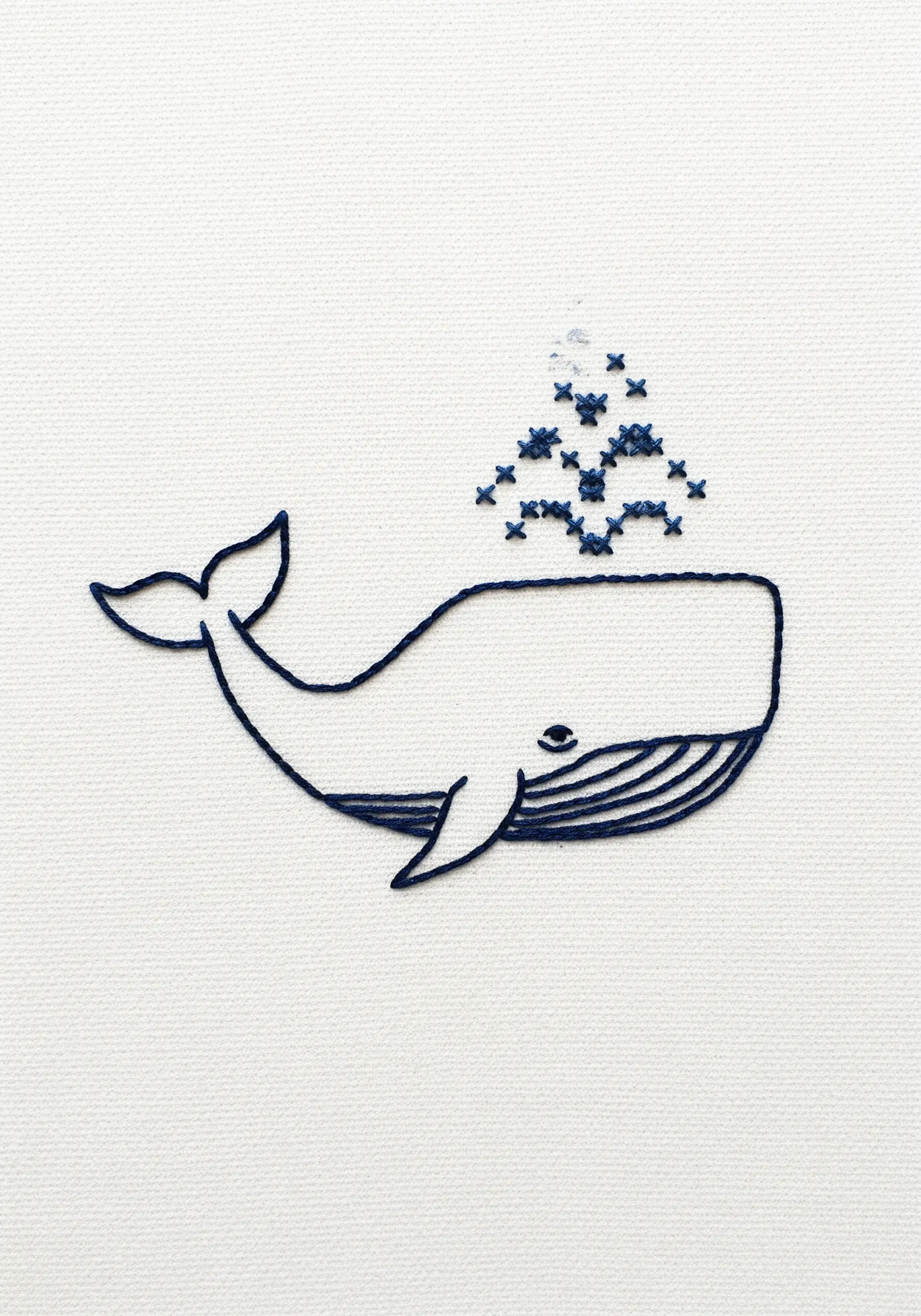 Line art embroidery of a whale with cross-stitch water spray details