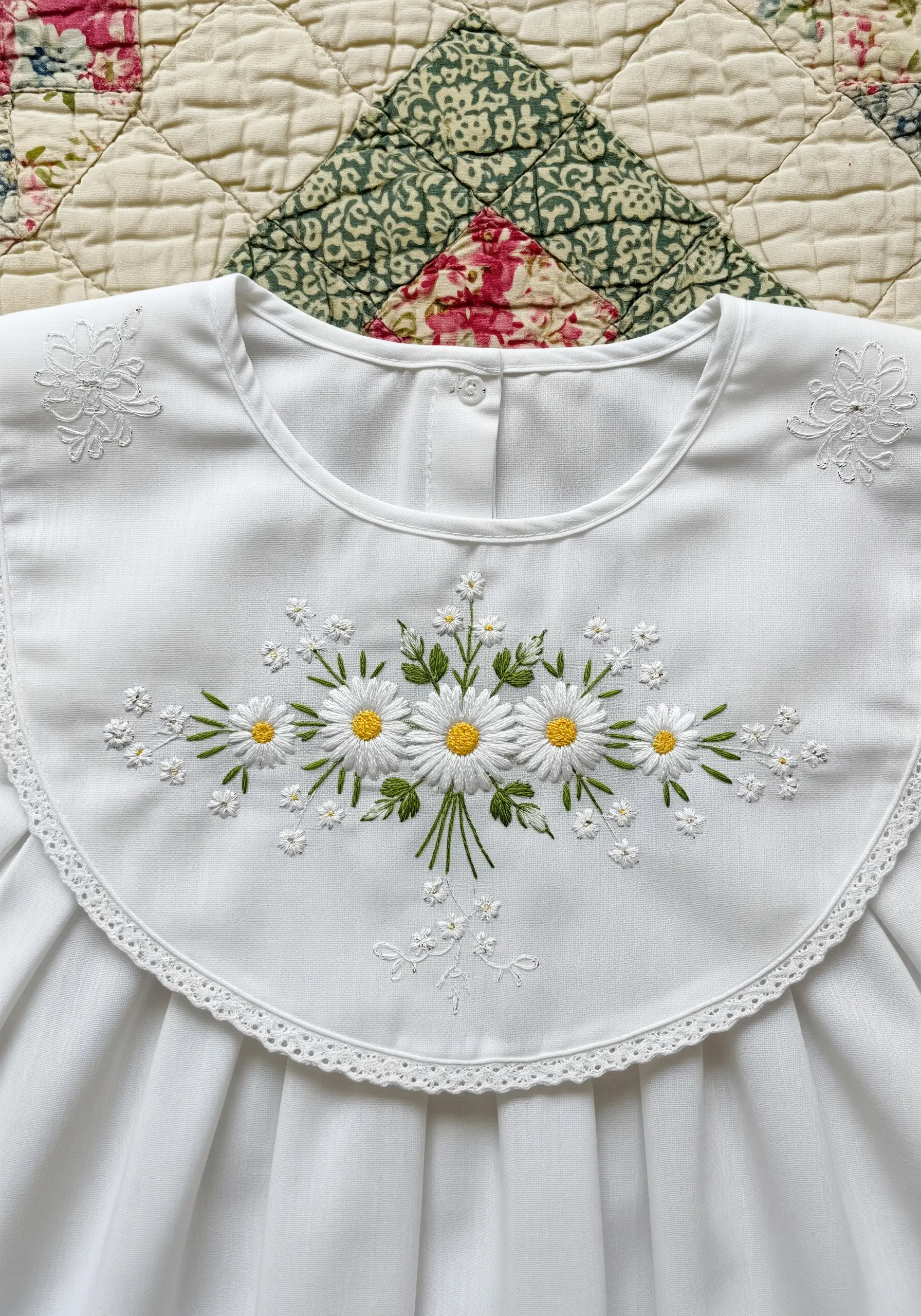 Embroidered daisies and delicate whitework on the collar of a white child's dress.
