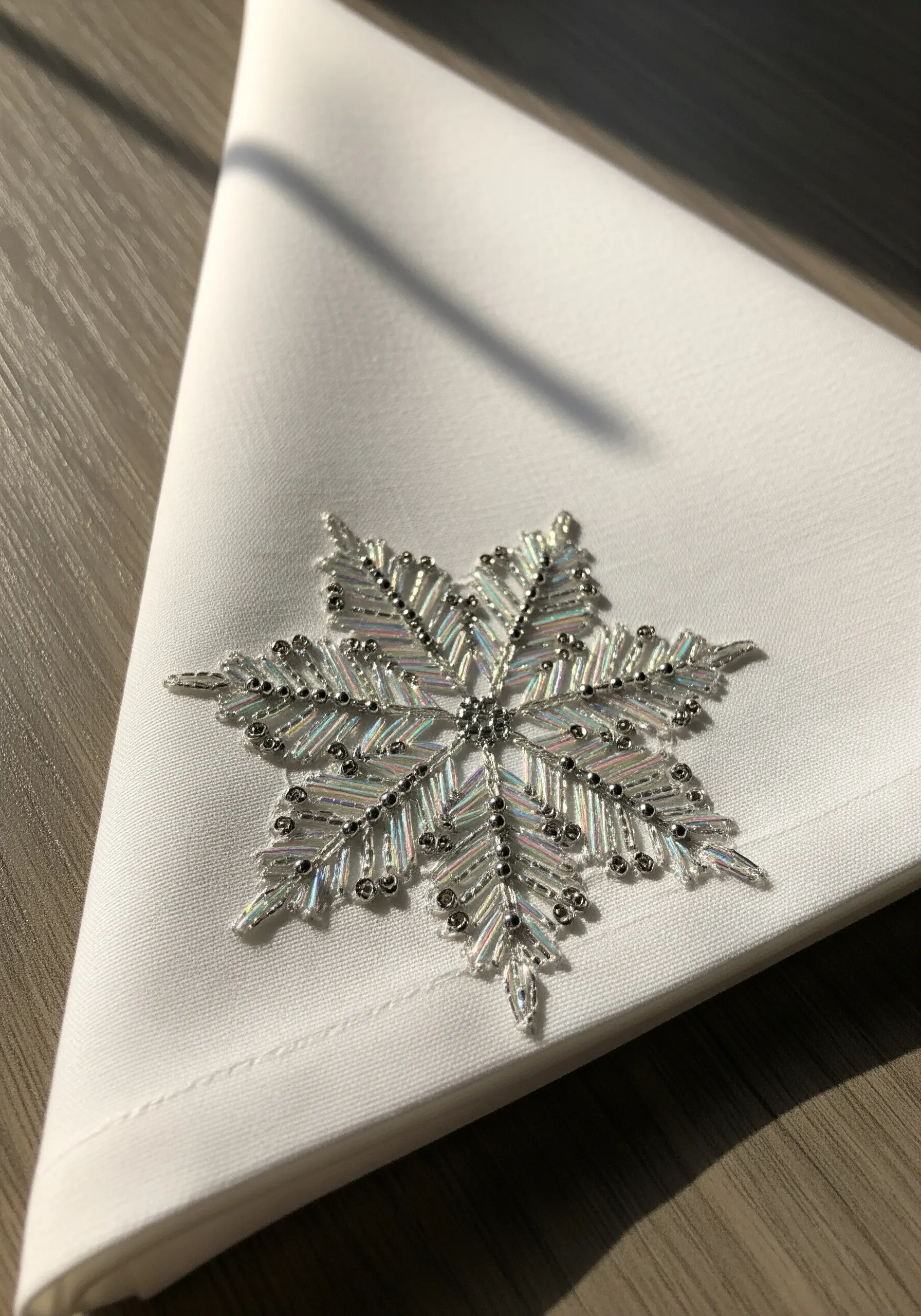 An intricate snowflake made entirely of silver and iridescent beads on a white napkin.
