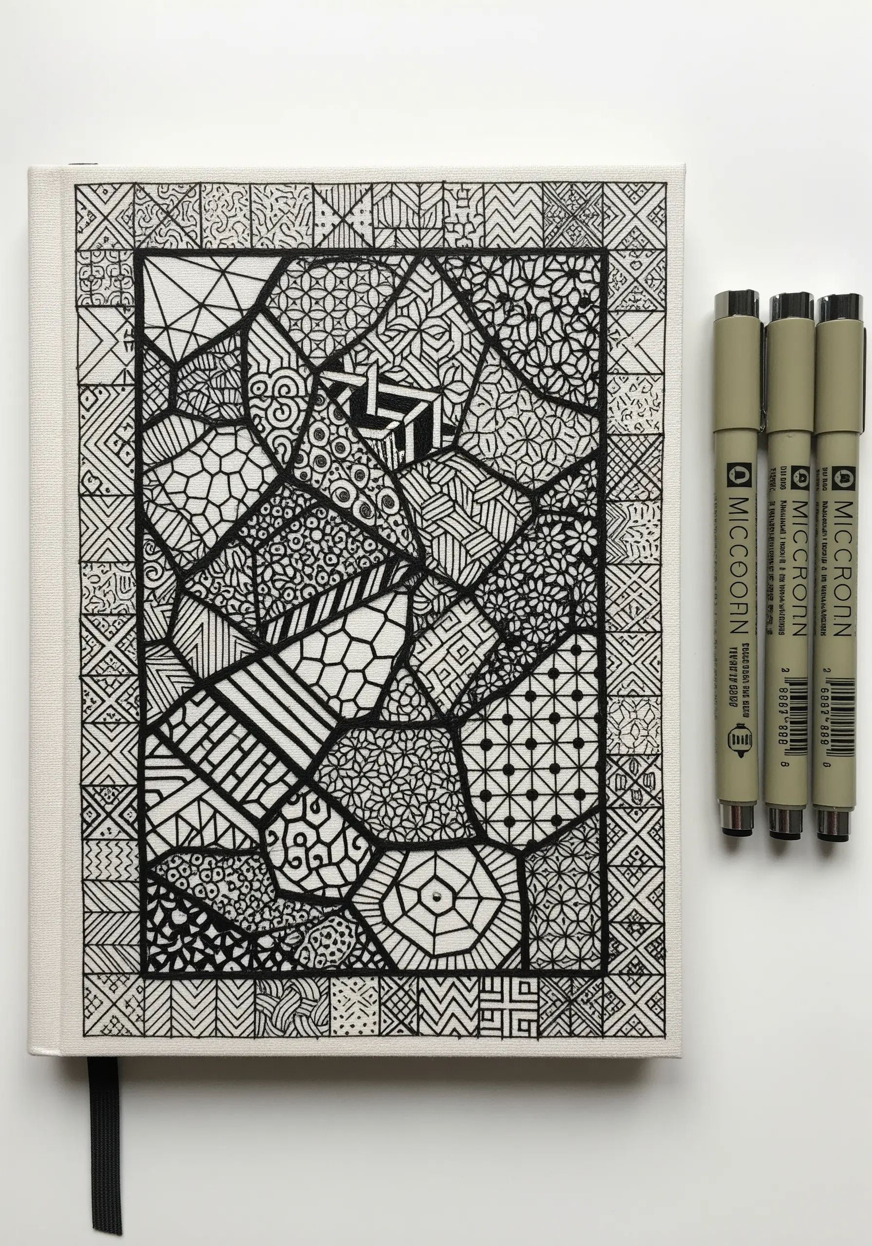 A black ink zentangle design on a journal cover, with some sections filled with black embroidery.