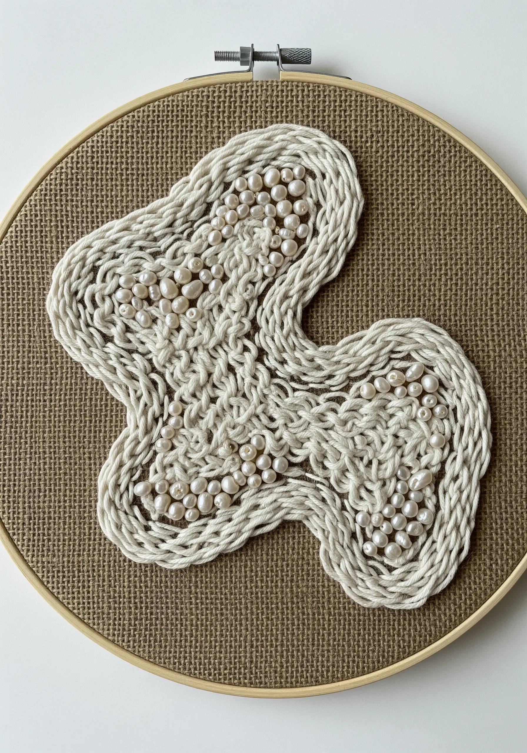 An abstract shape on burlap made with couched cord and filled with small white pearls.